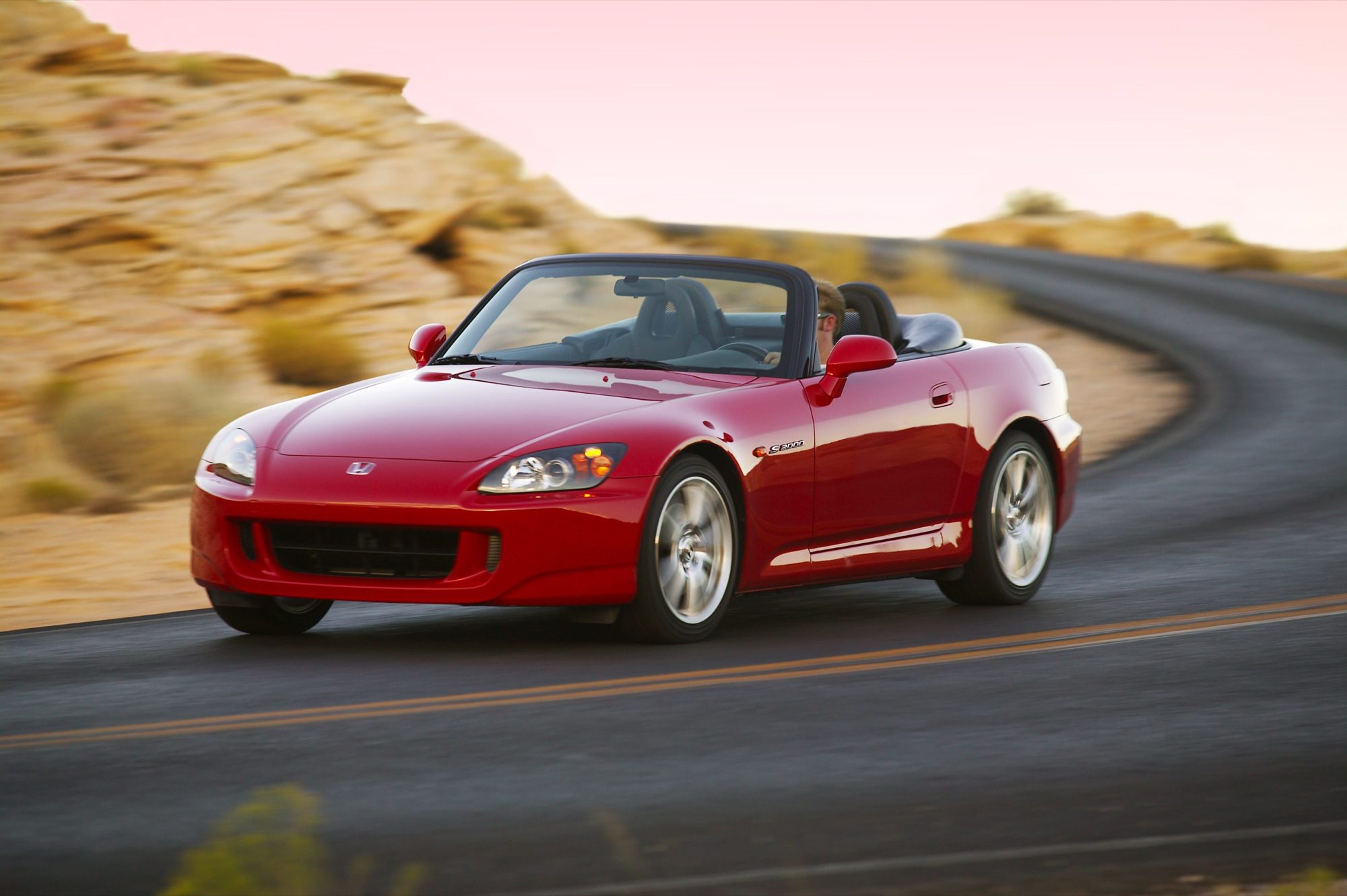 Red 2004 Honda S2000 with the top down driving on a winding desert road