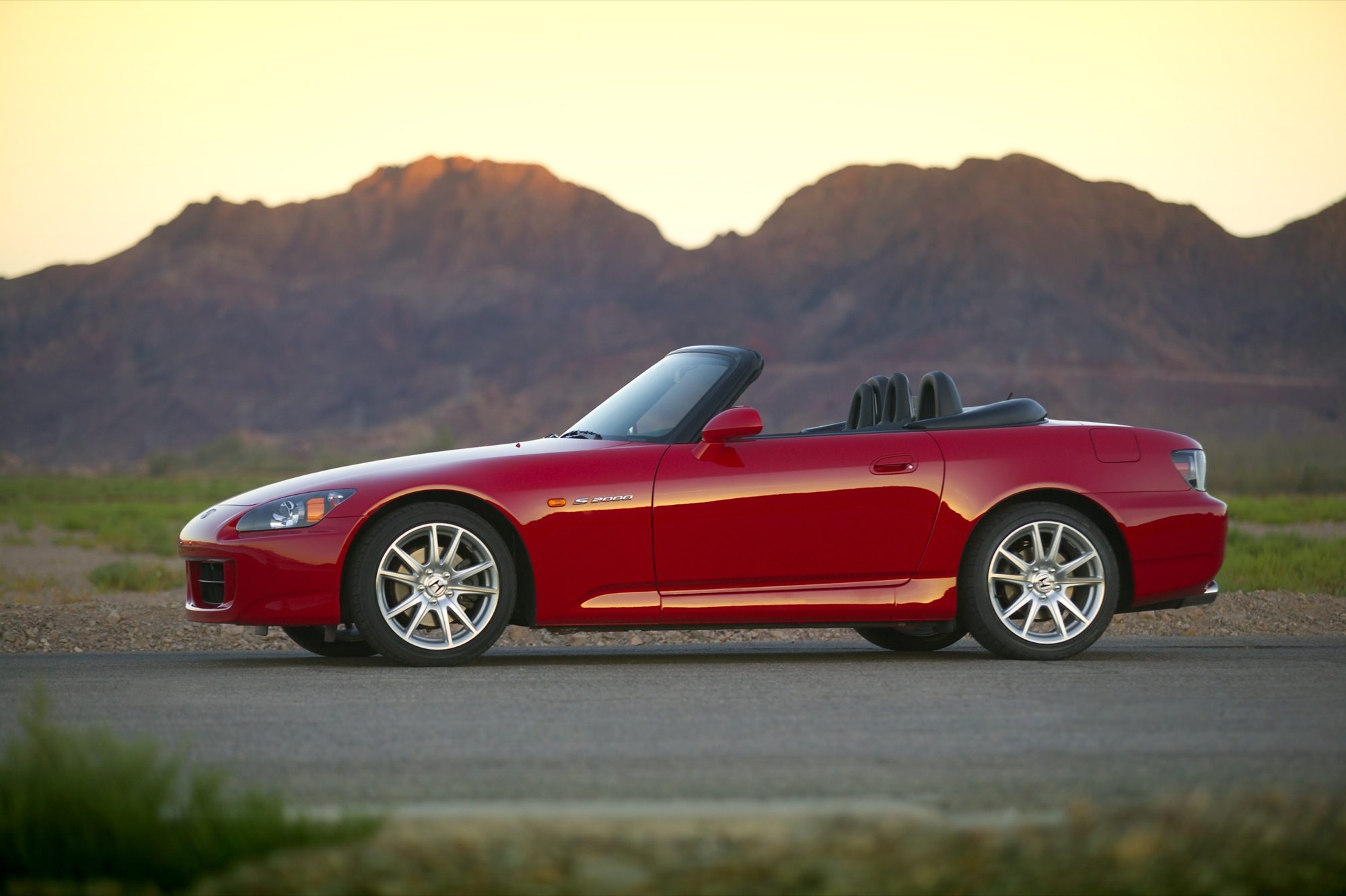 Side profile of a red 2004 Honda S2000 with its black soft top lowered