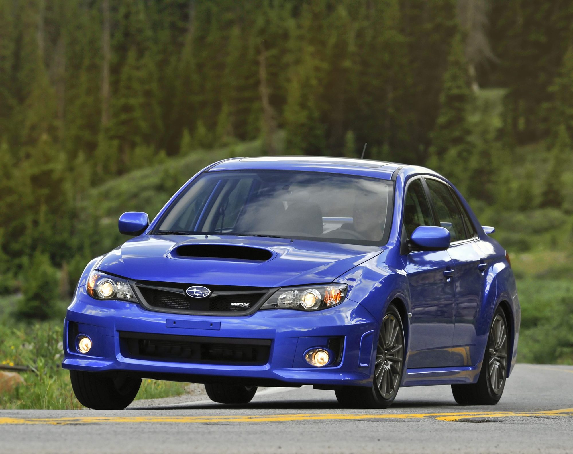 Blue 2011 Subaru Impreza WRX sedan cornering on a mountain road