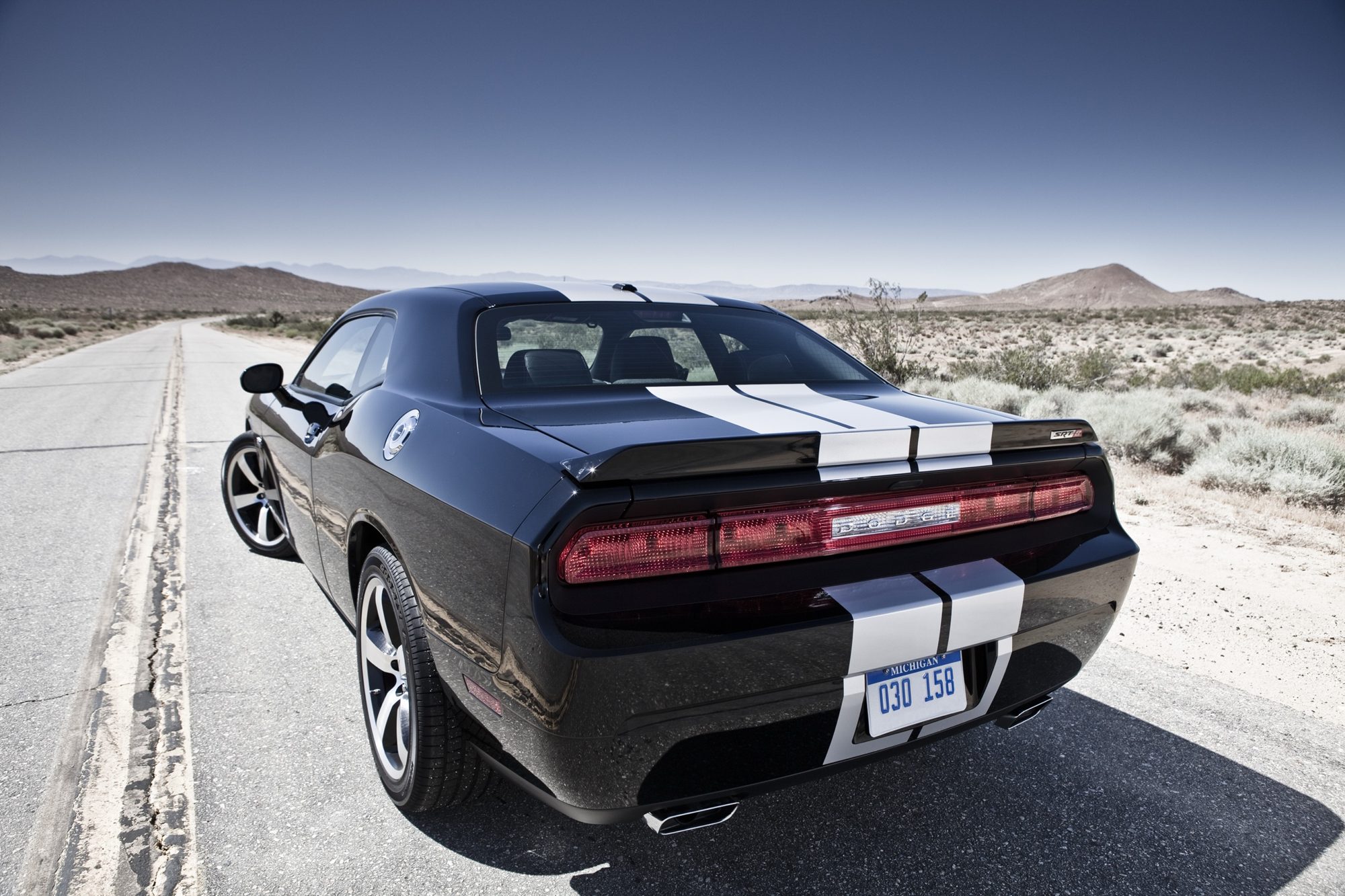 Rear three-quarter view of a black 2012 Dodge Challenger SRT8 392 with silver stripes and dual exhaust outlets on a desert road