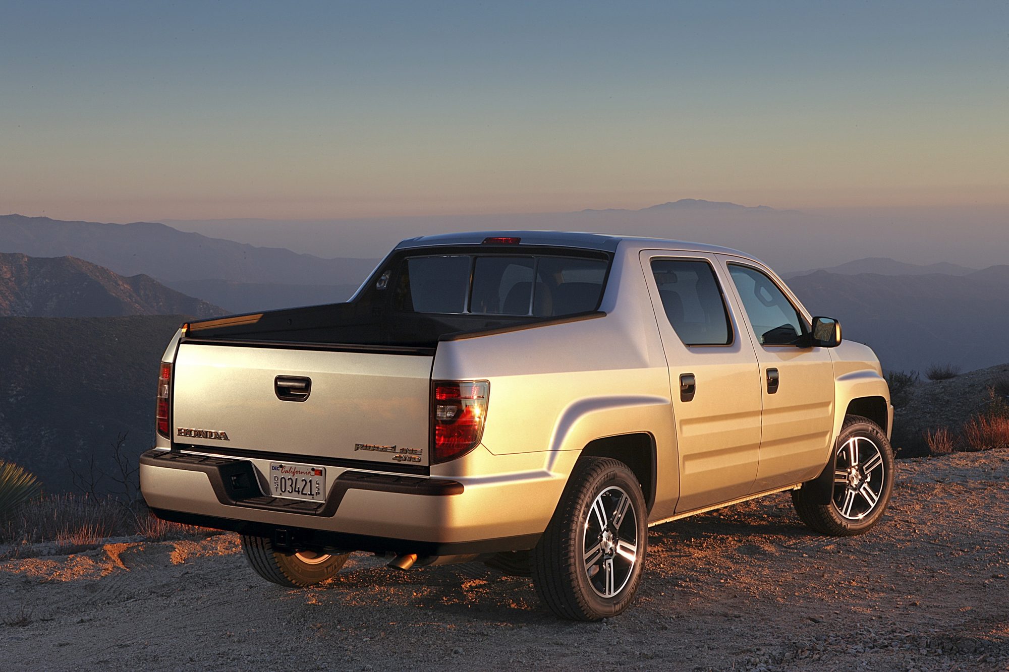 Rear three-quarter view of a silver 2012 Honda Ridgeline Sport at sunset in the mountains