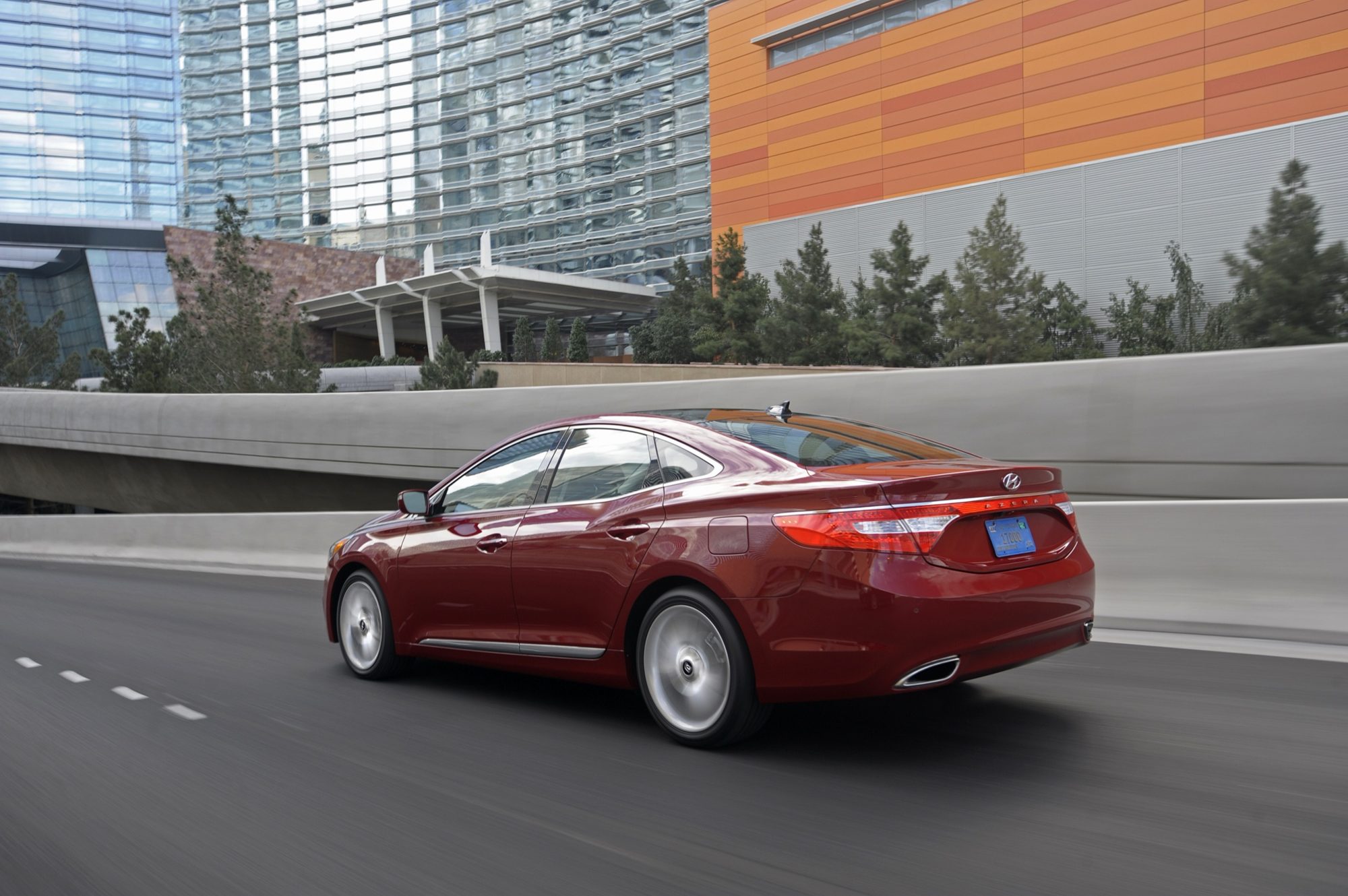 Red 2012 Hyundai Azera driving on an elevated city road, seen from the rear three-quarter