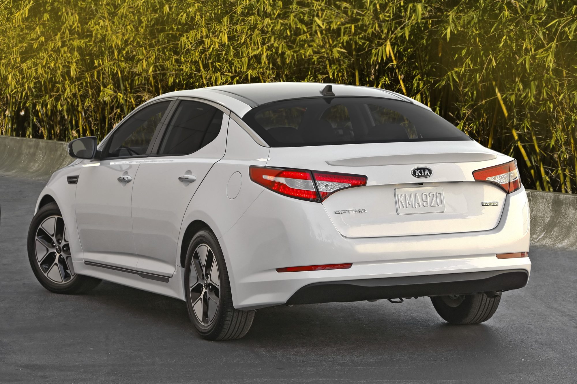 Rear three-quarter view of a white 2012 Kia Optima Hybrid showing the lip spoiler and Hybrid badge