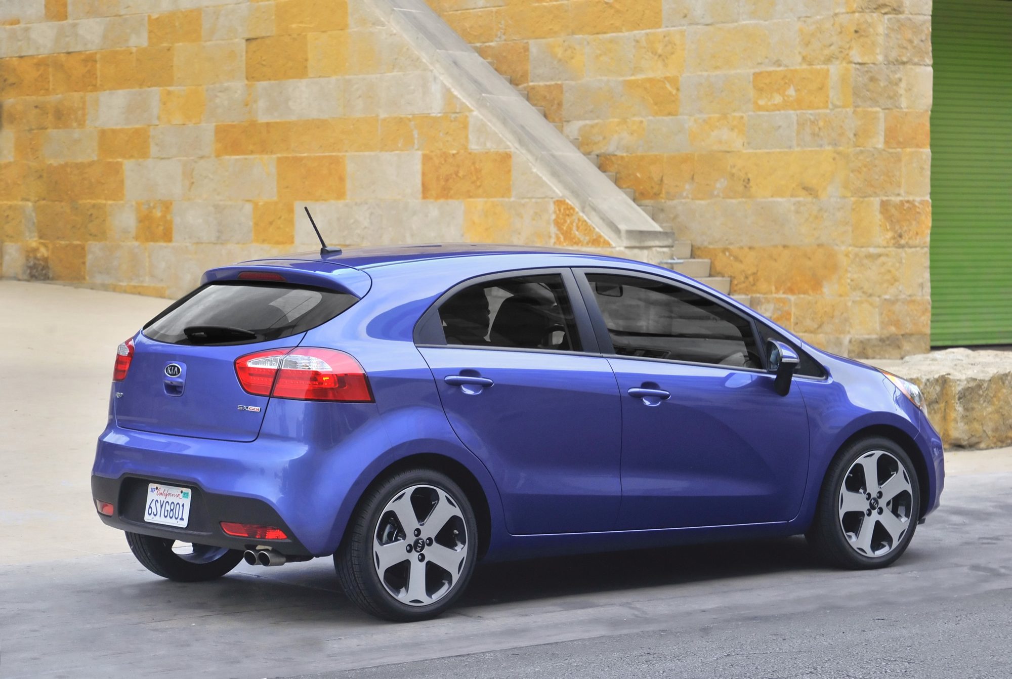 Rear three-quarter view of a blue 2012 Kia Rio SX 5-door hatchback with twin exhaust tips