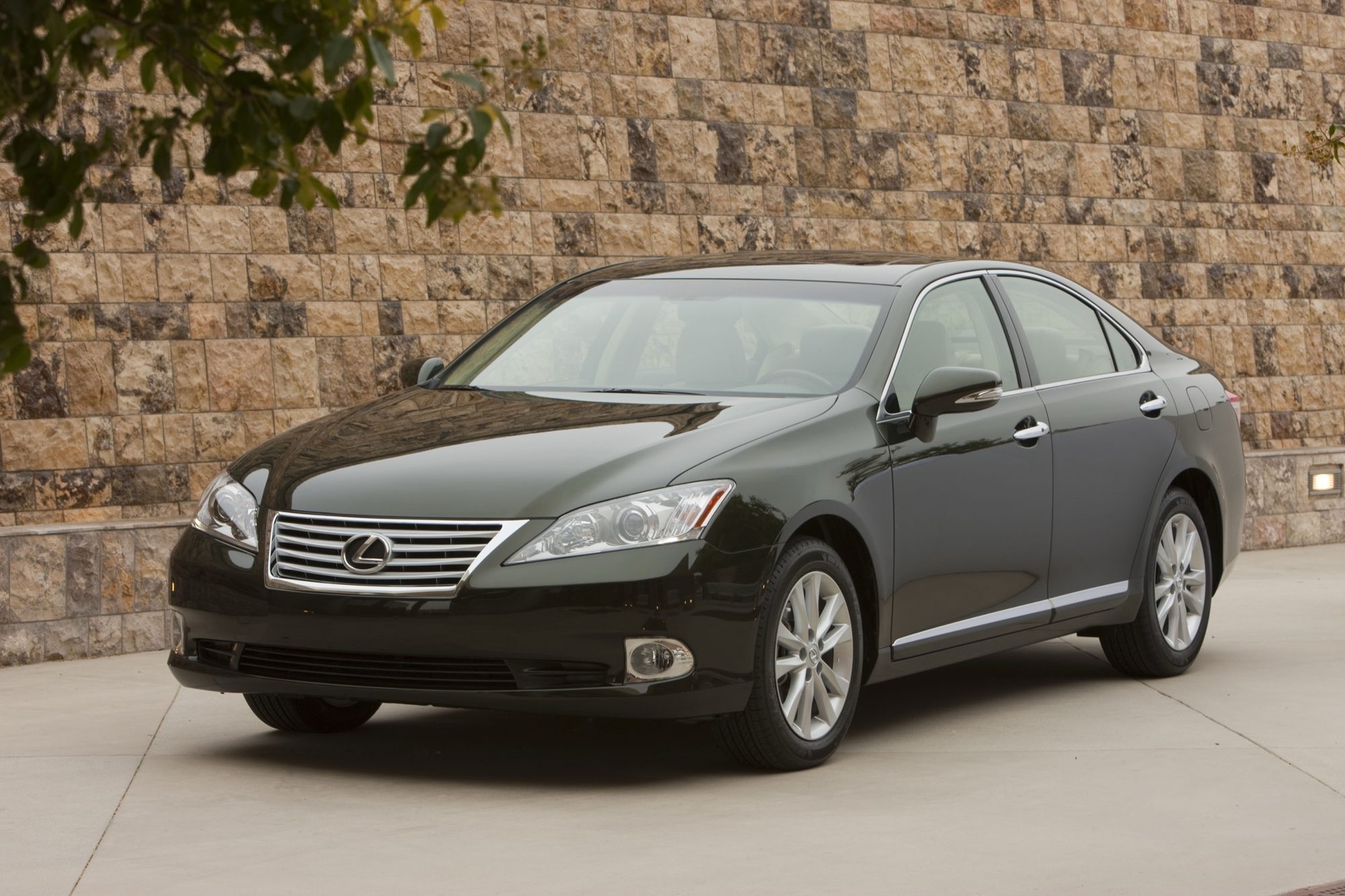 Front three-quarter view of a dark green 2012 Lexus ES 350 sedan parked by a stone wall
