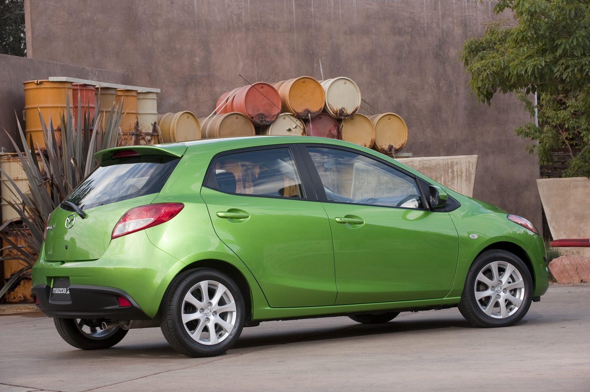 Rear three-quarter view of a green 2012 Mazda2 Touring with its roof spoiler