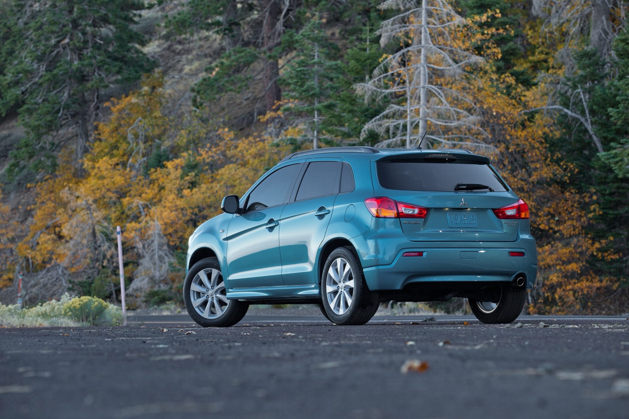 Rear three-quarter view of a blue 2012 Mitsubishi Outlander Sport SE with autumn trees behind