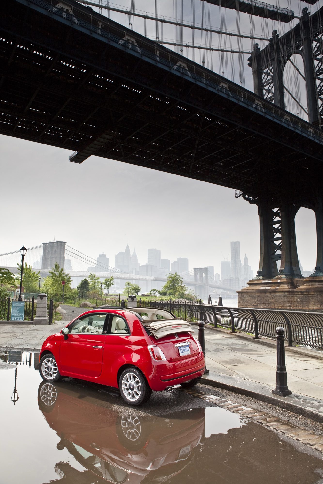 Rear three-quarter view of a red 2013 Fiat 500c with its cloth top folded back, parked by the East River in New York