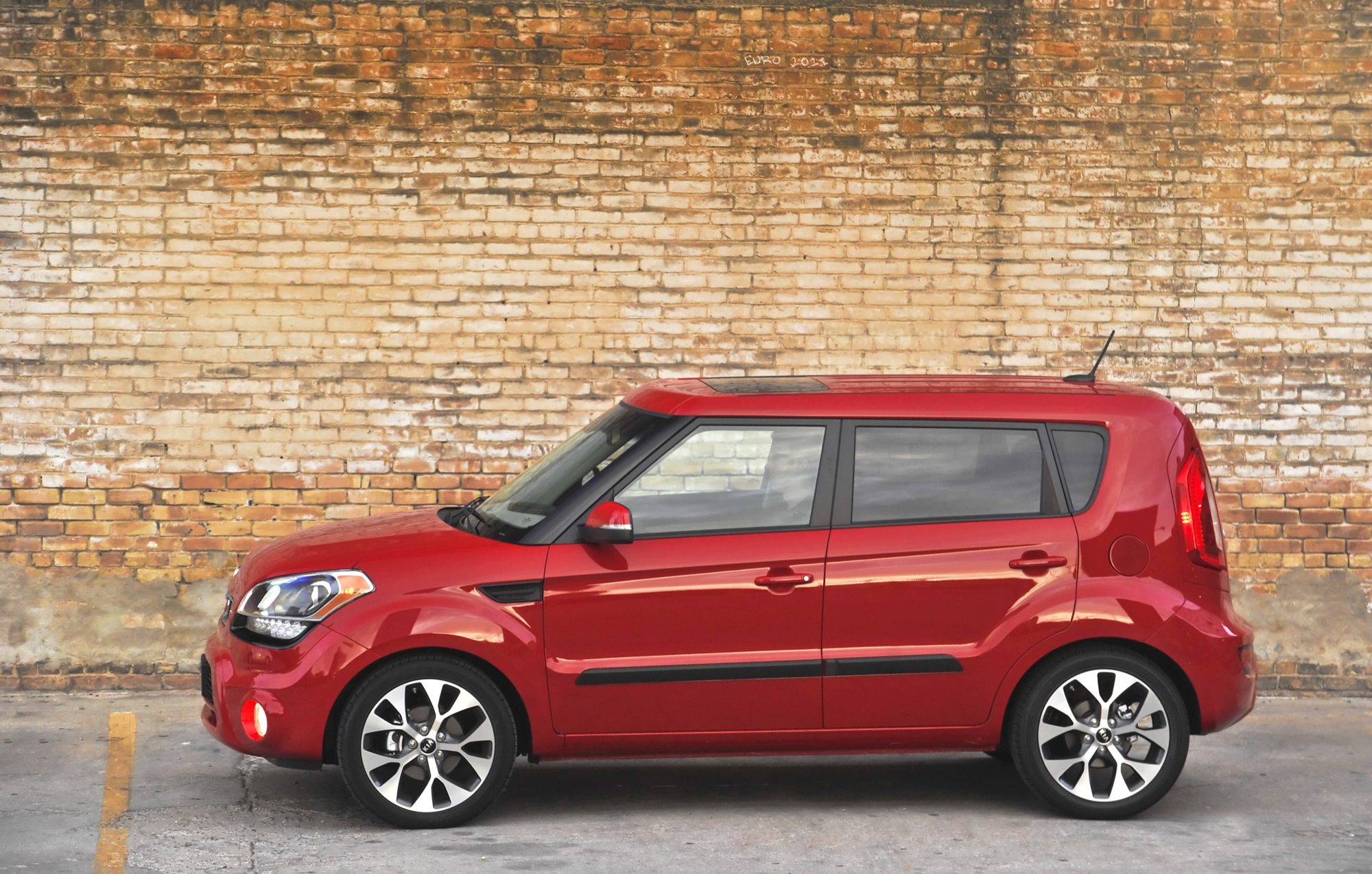 Side profile of a red 2013 Kia Soul in front of a brick wall
