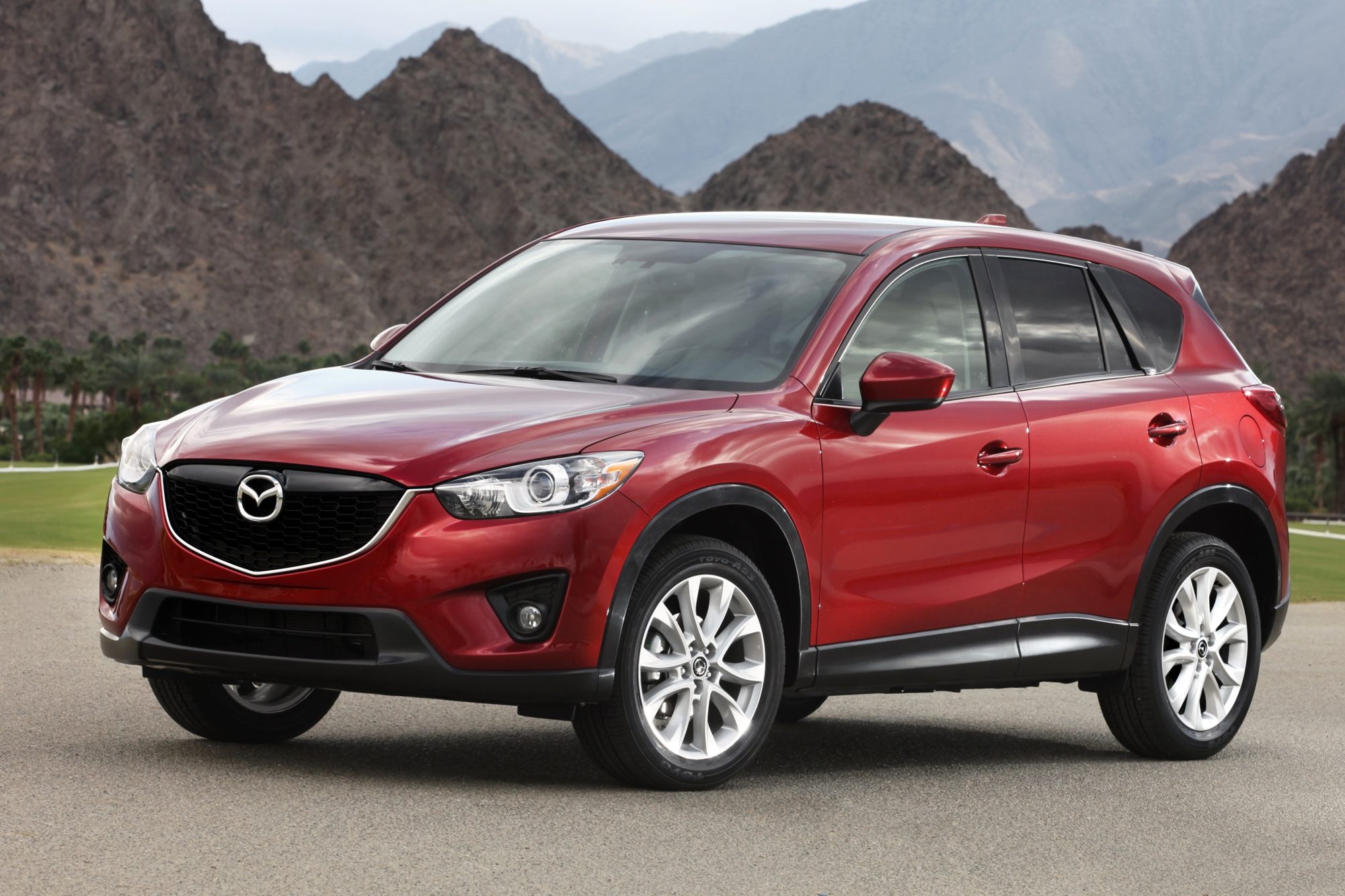 Front three-quarter view of a red 2013 Mazda CX-5 parked in front of desert mountains