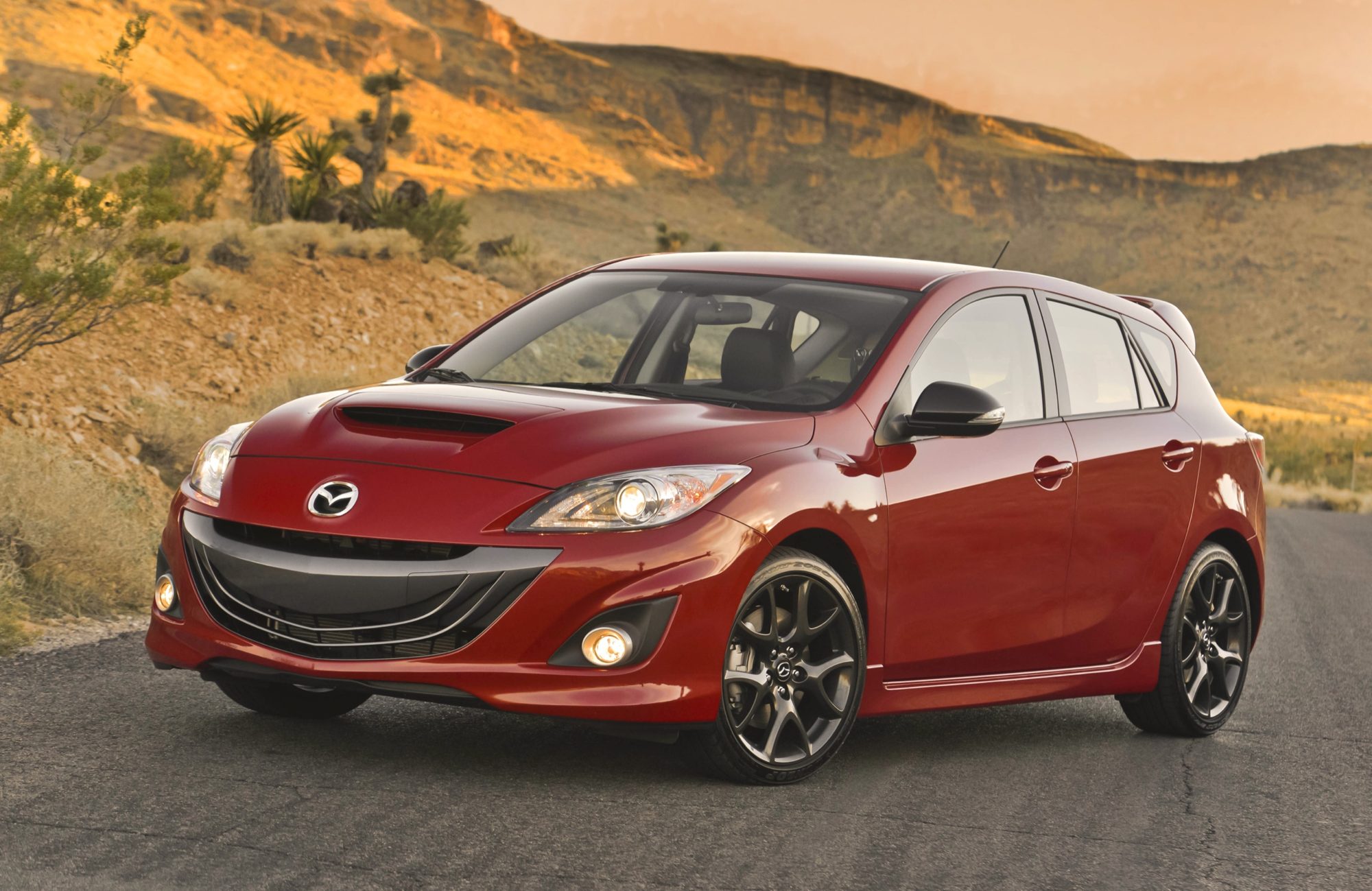 Front three-quarter view of a red 2013 Mazdaspeed3 hatchback on a desert road