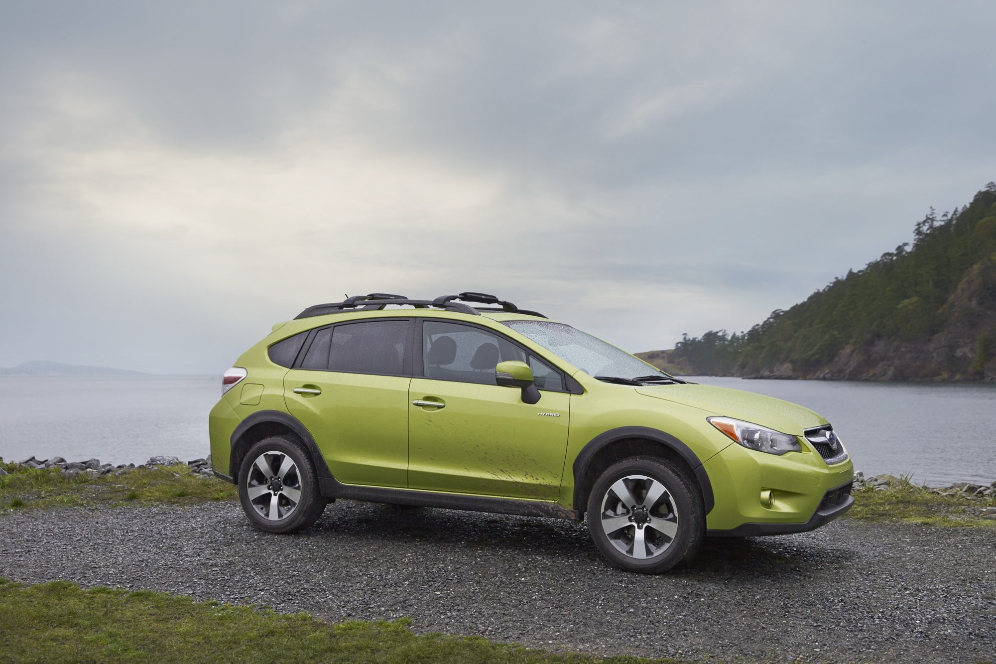 Front three-quarter view of a Plasma Green Pearl 2014 Subaru XV Crosstrek Hybrid parked on a gravel shoreline