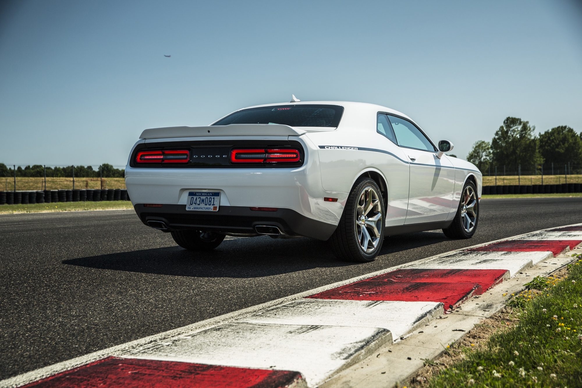 Rear three-quarter view of a white 2015 Dodge Challenger SXT Plus showing the full-width taillamps and rear spoiler