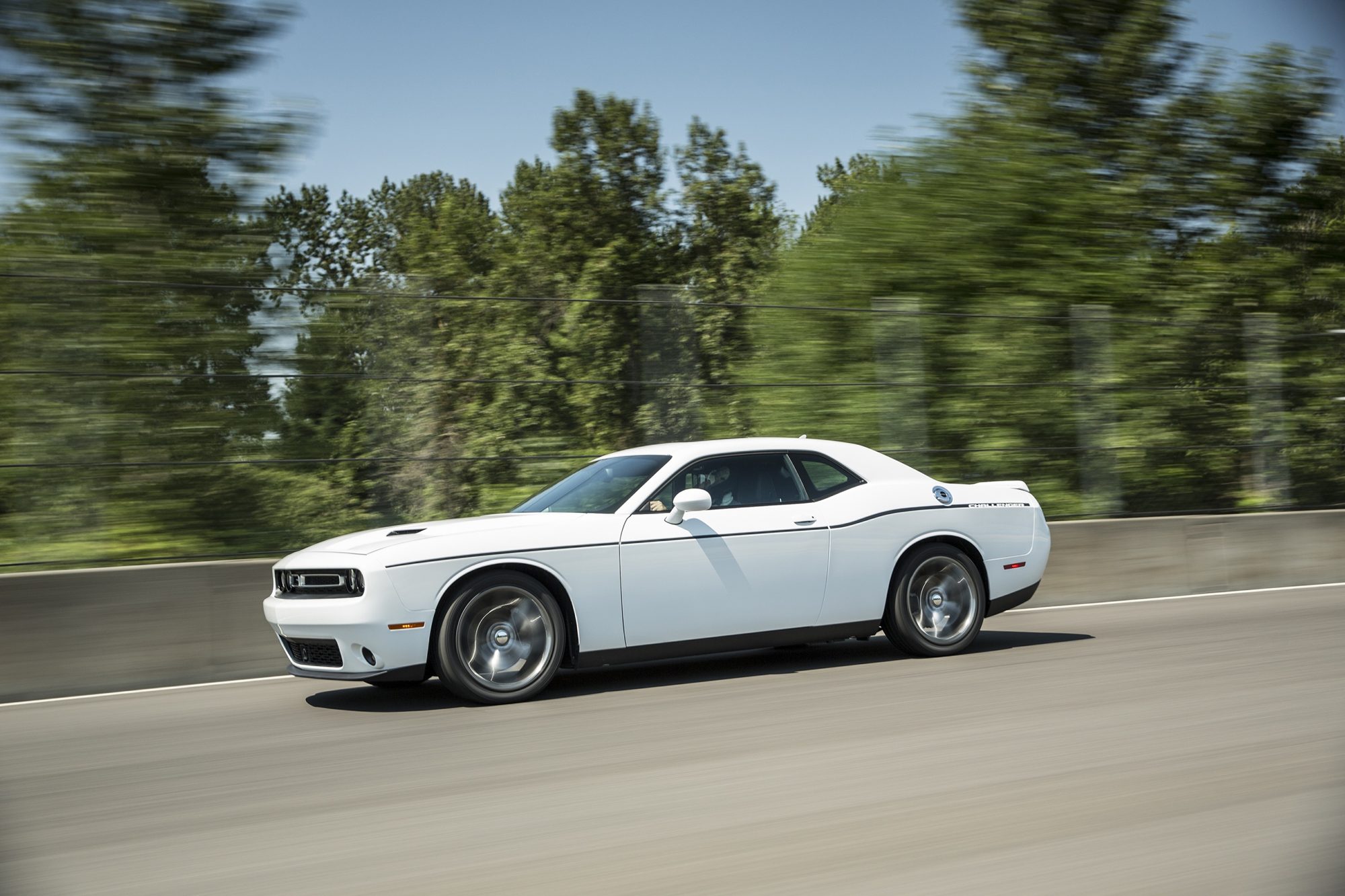White 2015 Dodge Challenger SXT Plus driving past trees, seen from the side