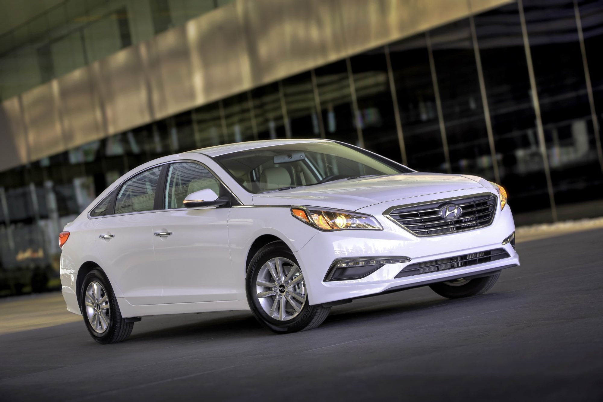 Front three-quarter view of a white 2015 Hyundai Sonata Eco parked by a glass building