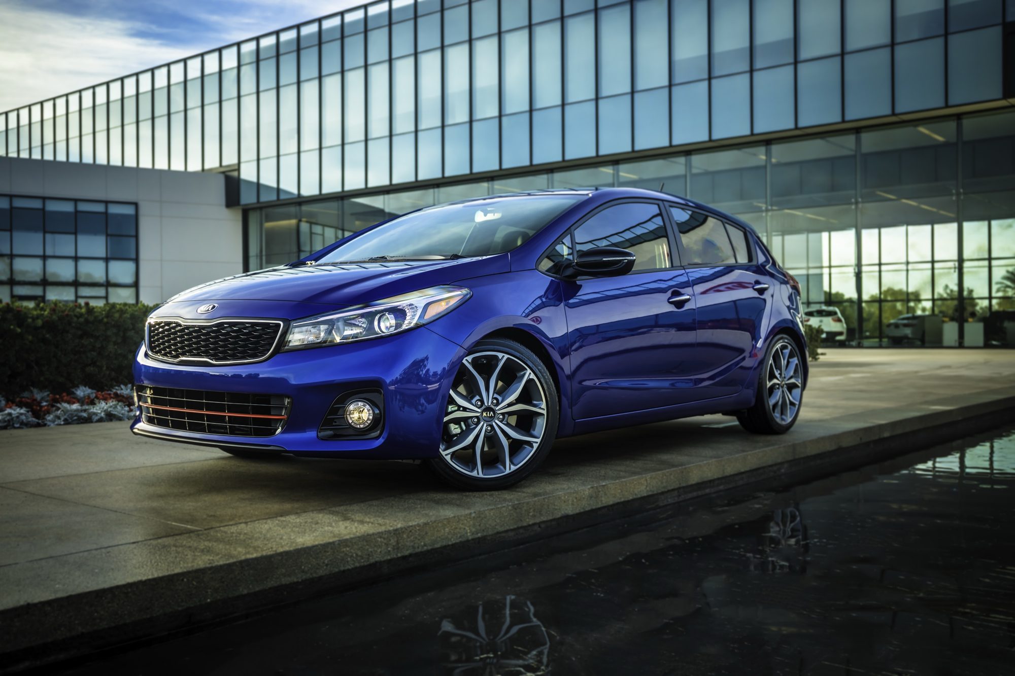 Front three-quarter view of a blue 2017 Kia Forte5 SX parked by a reflecting pool