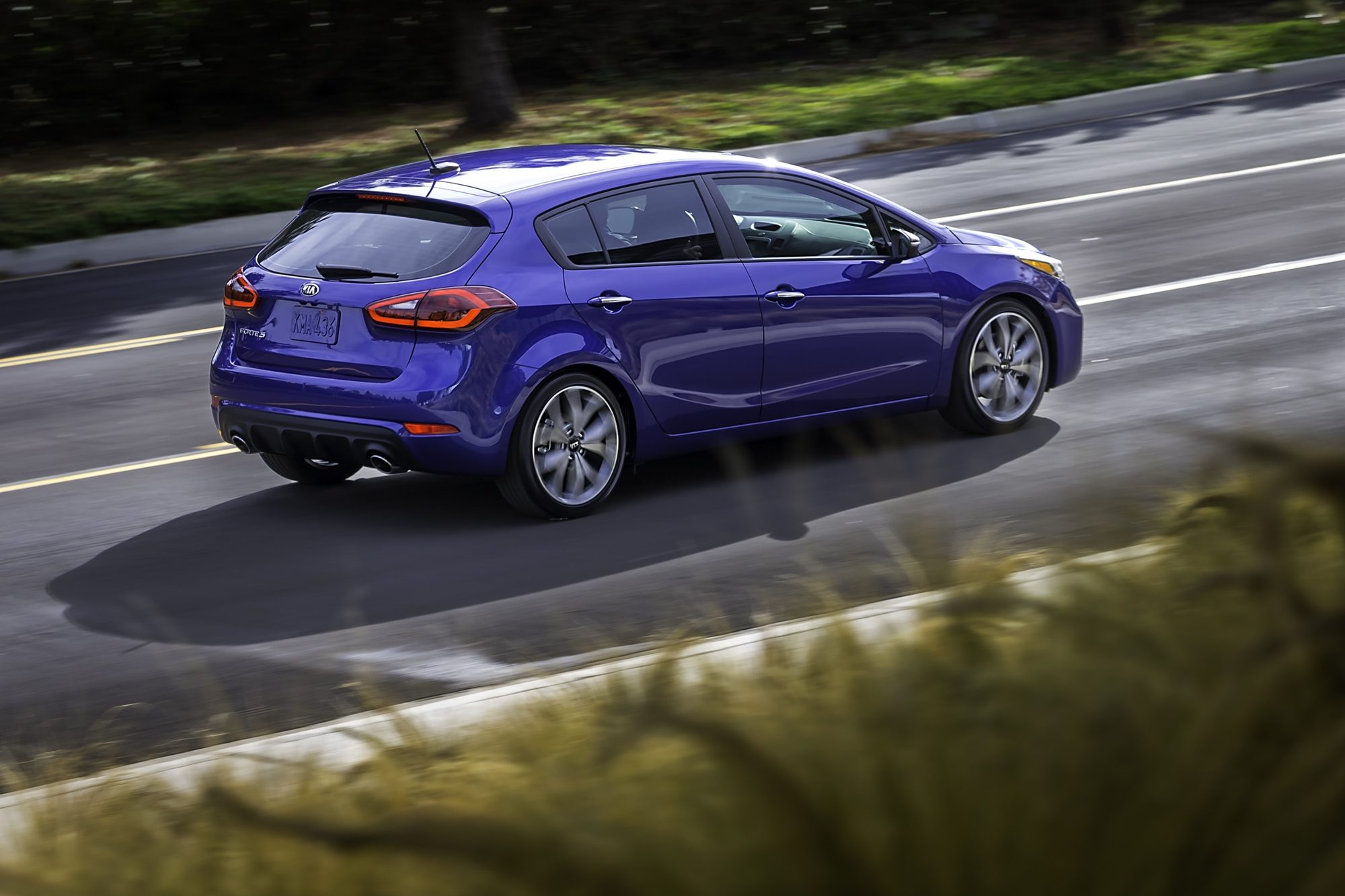 Rear three-quarter view of a blue 2017 Kia Forte5 SX hatchback driving
