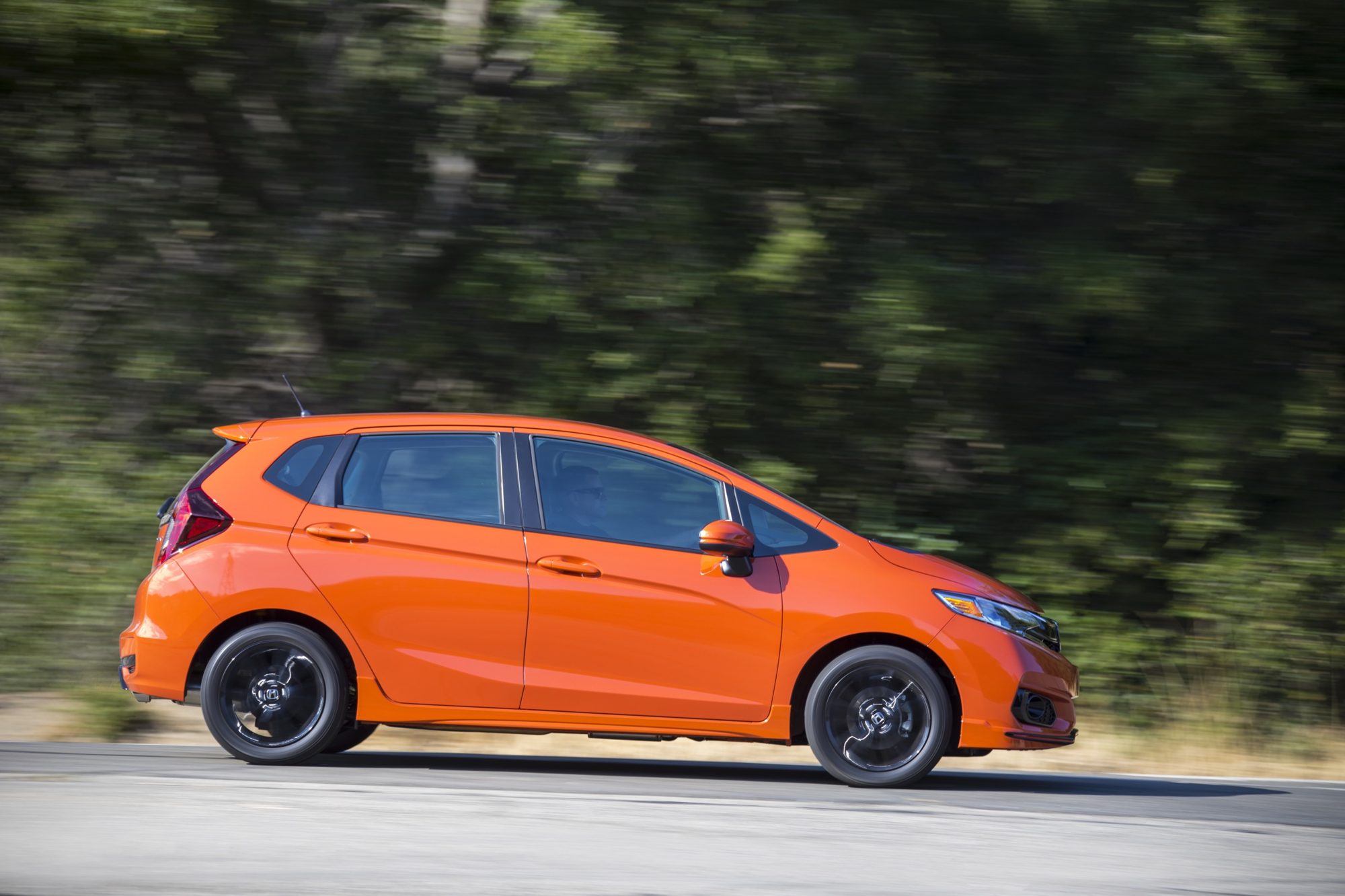 Side view of an Orange Fury 2018 Honda Fit Sport driving past trees