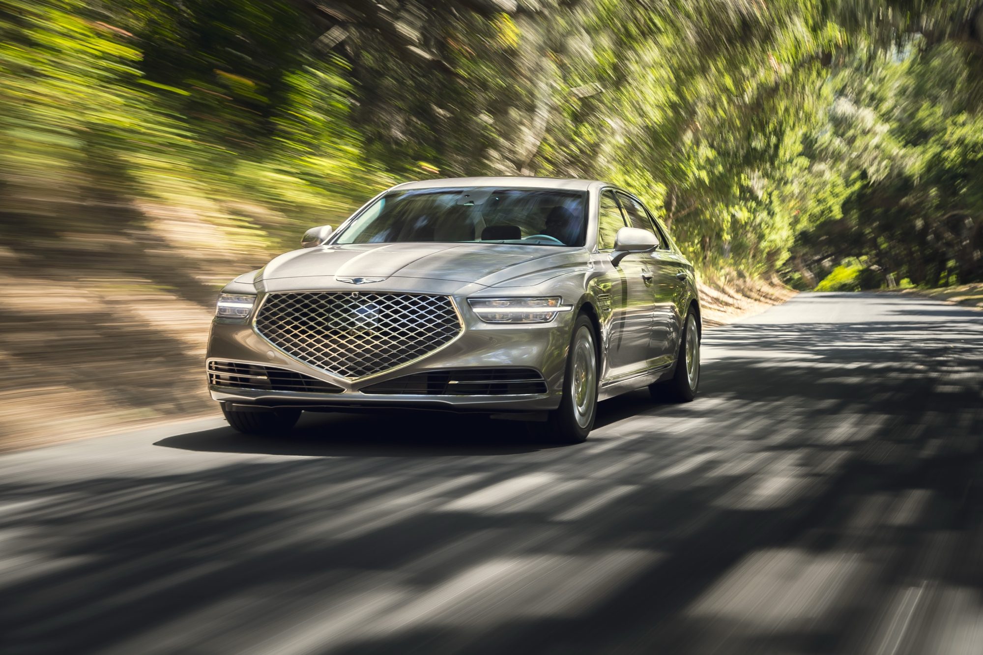 Front view of a 2020 Genesis G90 driving on a tree-lined road