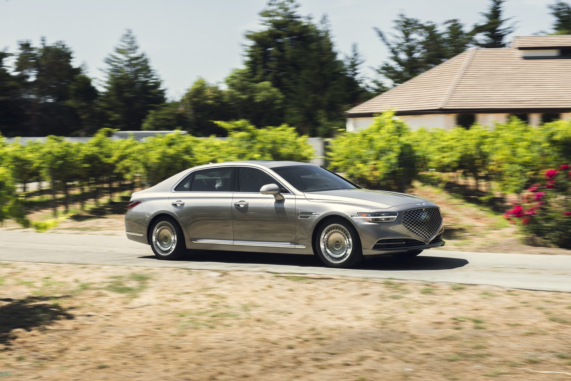 Side profile of a 2020 Genesis G90 in Gold Coast Silver driving past a vineyard