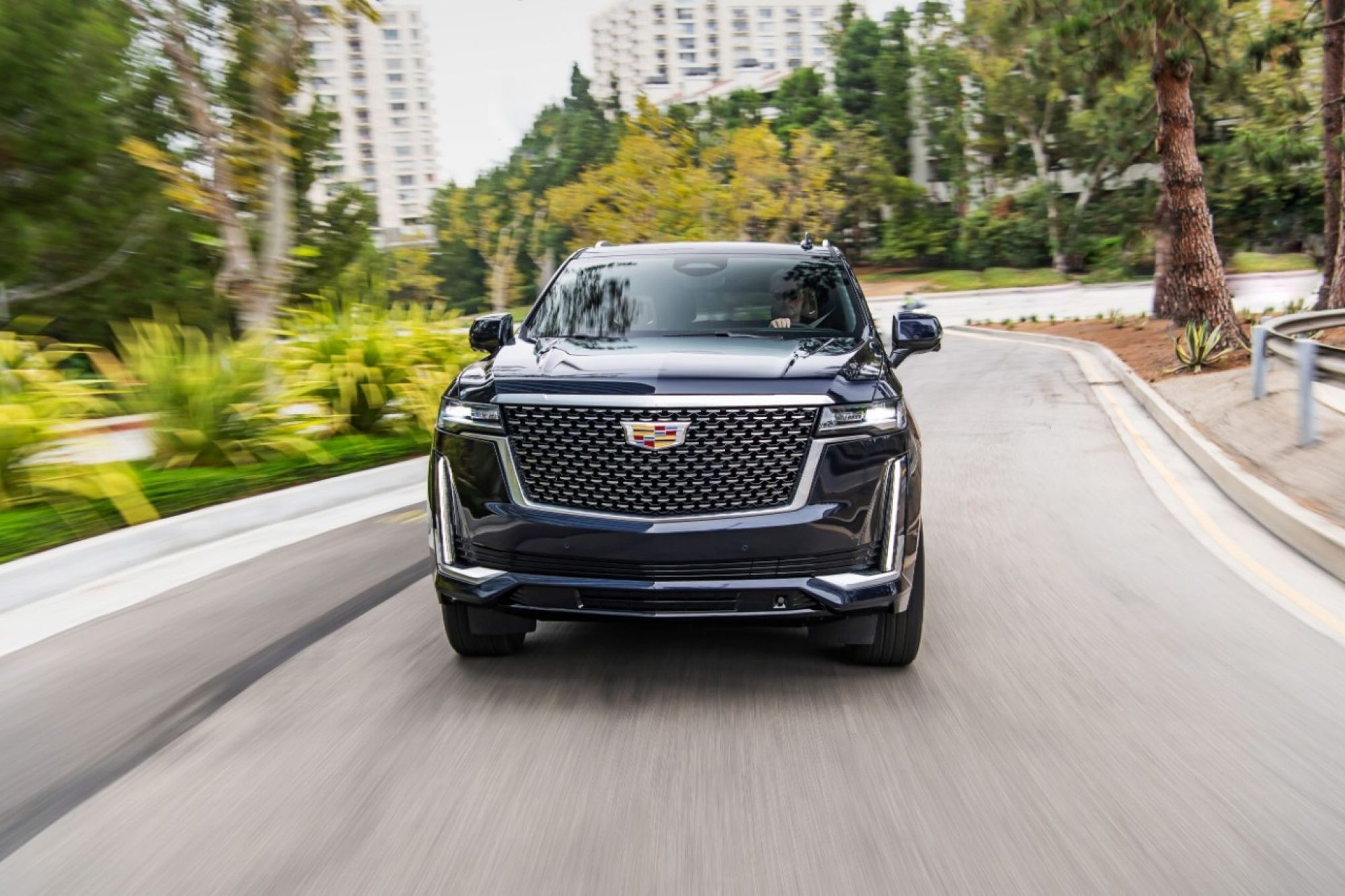 Front view of a dark 2021 Cadillac Escalade driving on a tree-lined road