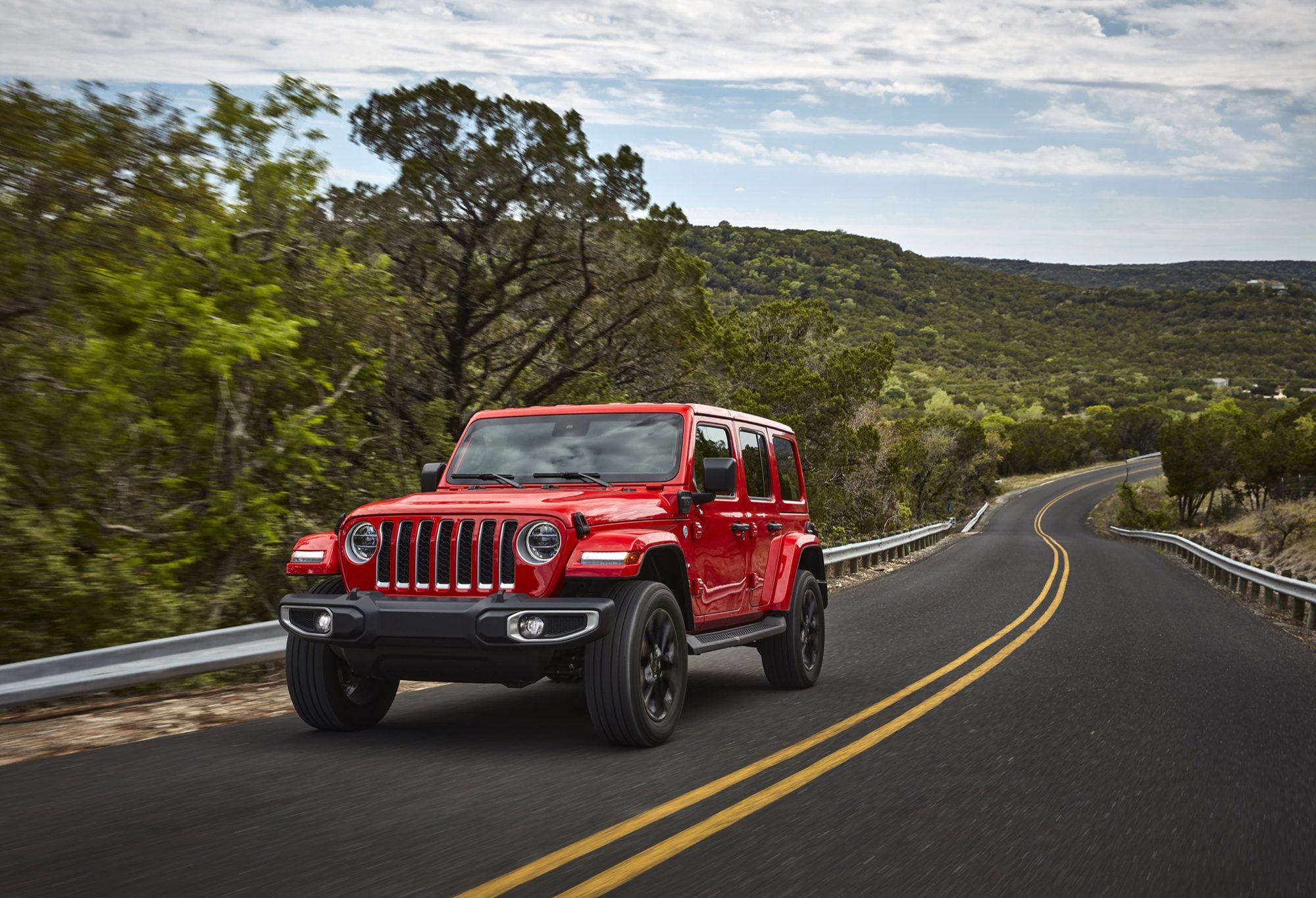 Red 2021 Jeep Wrangler Sahara 4xe driving on a winding road