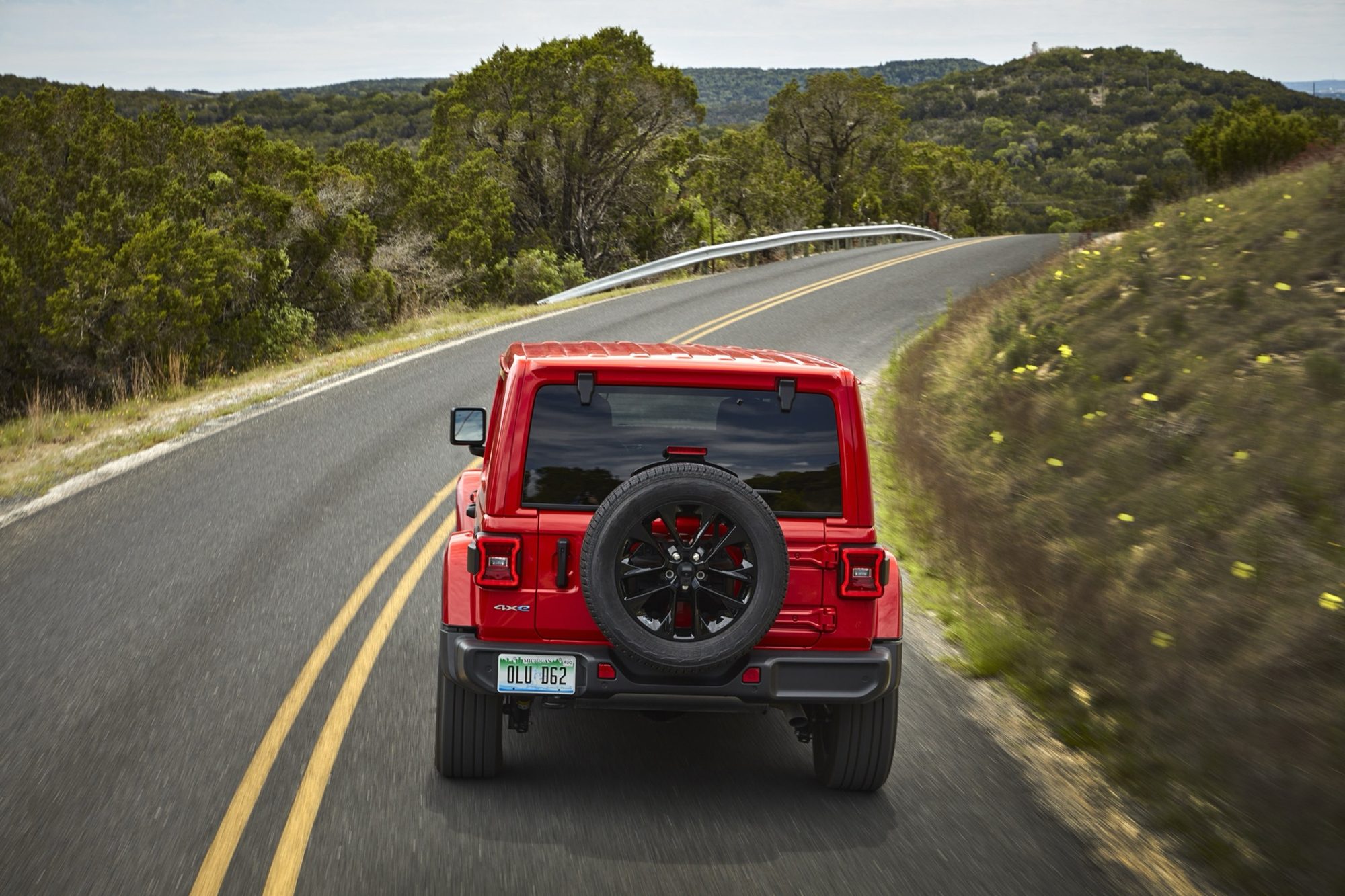 Red 2021 Jeep Wrangler Sahara 4xe driving away, rear view with spare tire