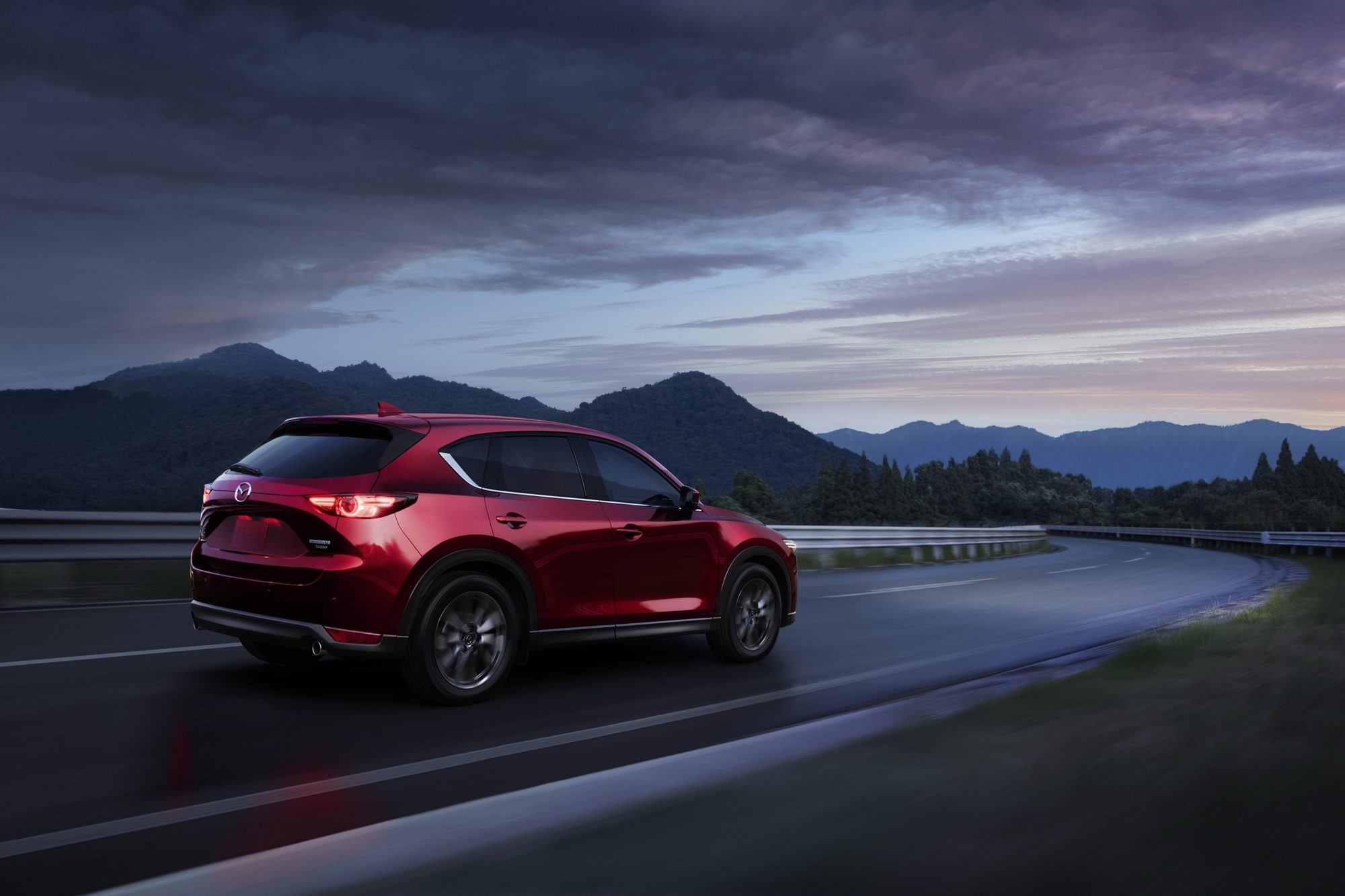 Rear three-quarter view of a red 2021 Mazda CX-5 on a mountain road at dusk