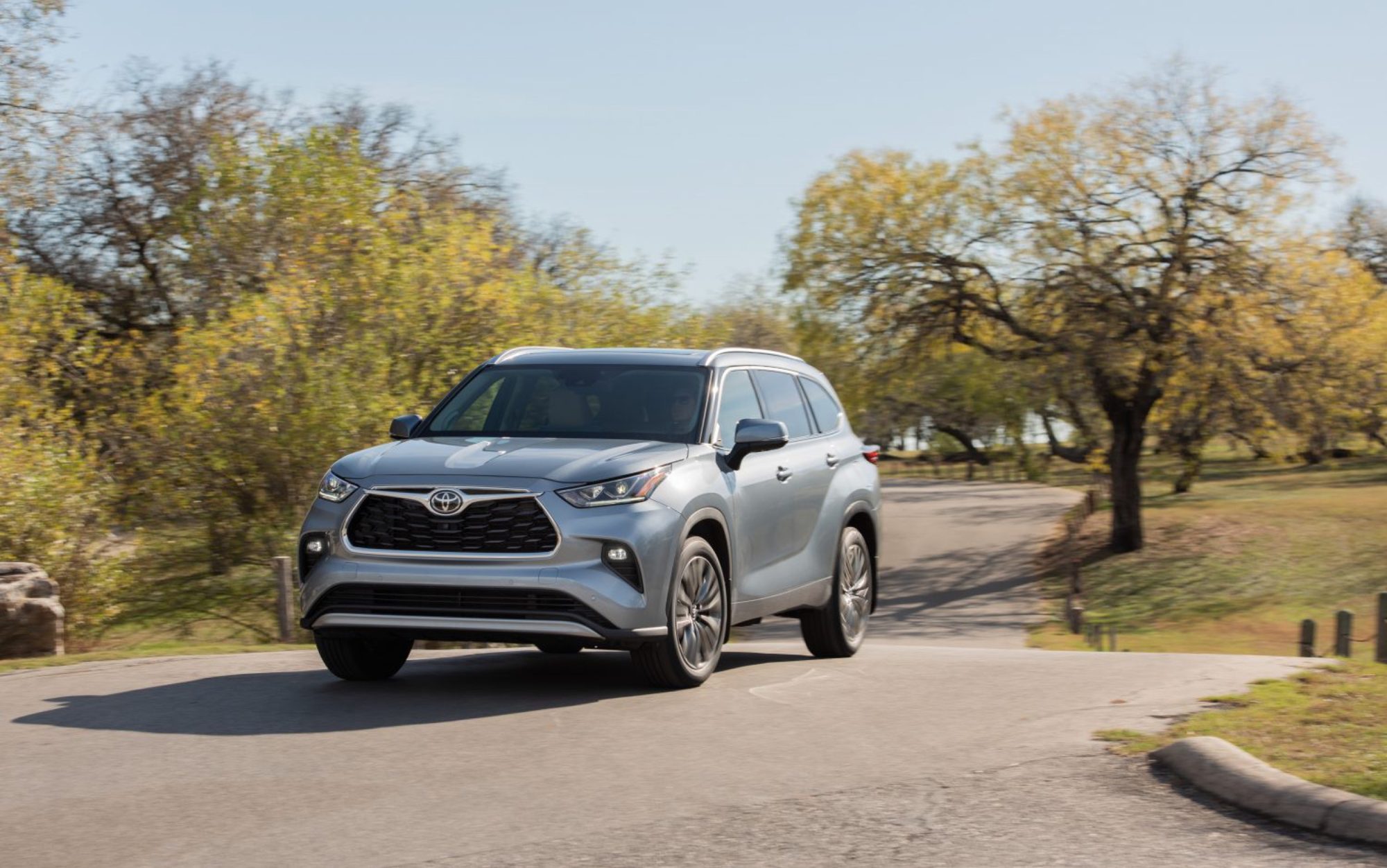 2022 Toyota Highlander Platinum AWD in Moon Dust driving on a park road, front three-quarter view
