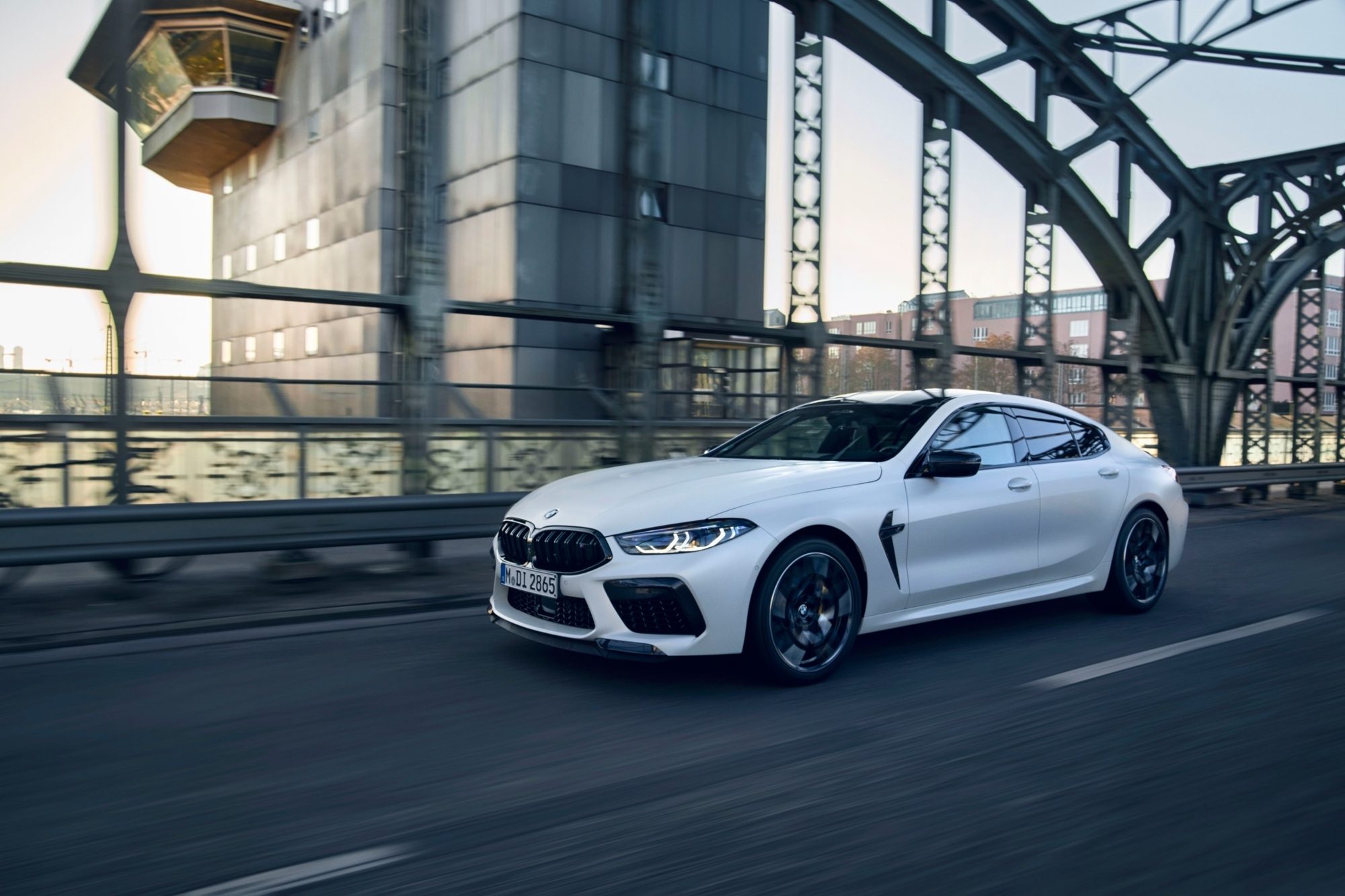 White 2023 BMW M8 Competition Gran Coupe driving across a steel bridge