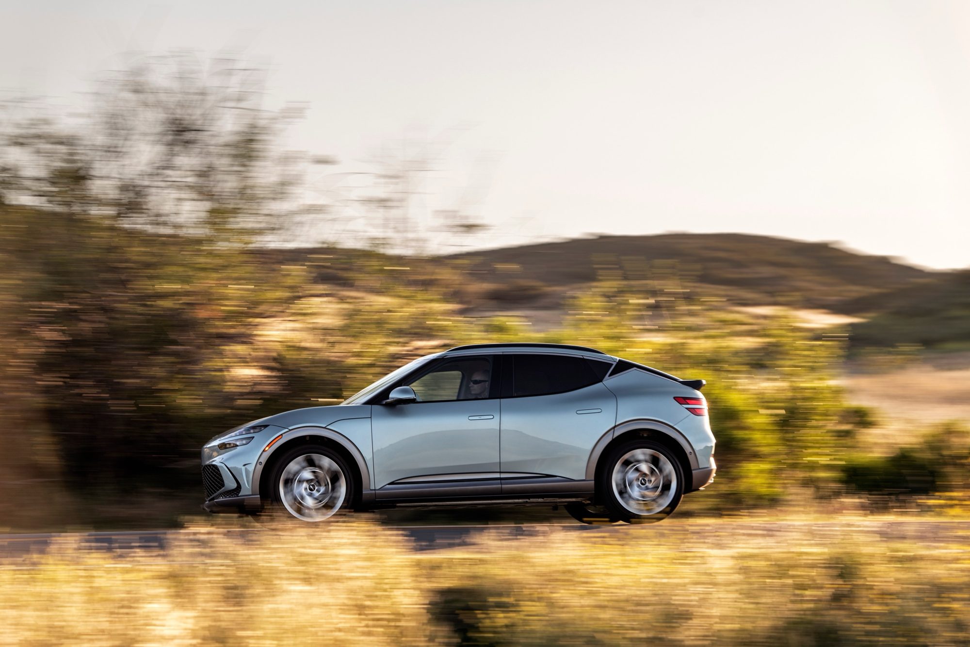 Silver 2023 Genesis GV60 driving past dry hills