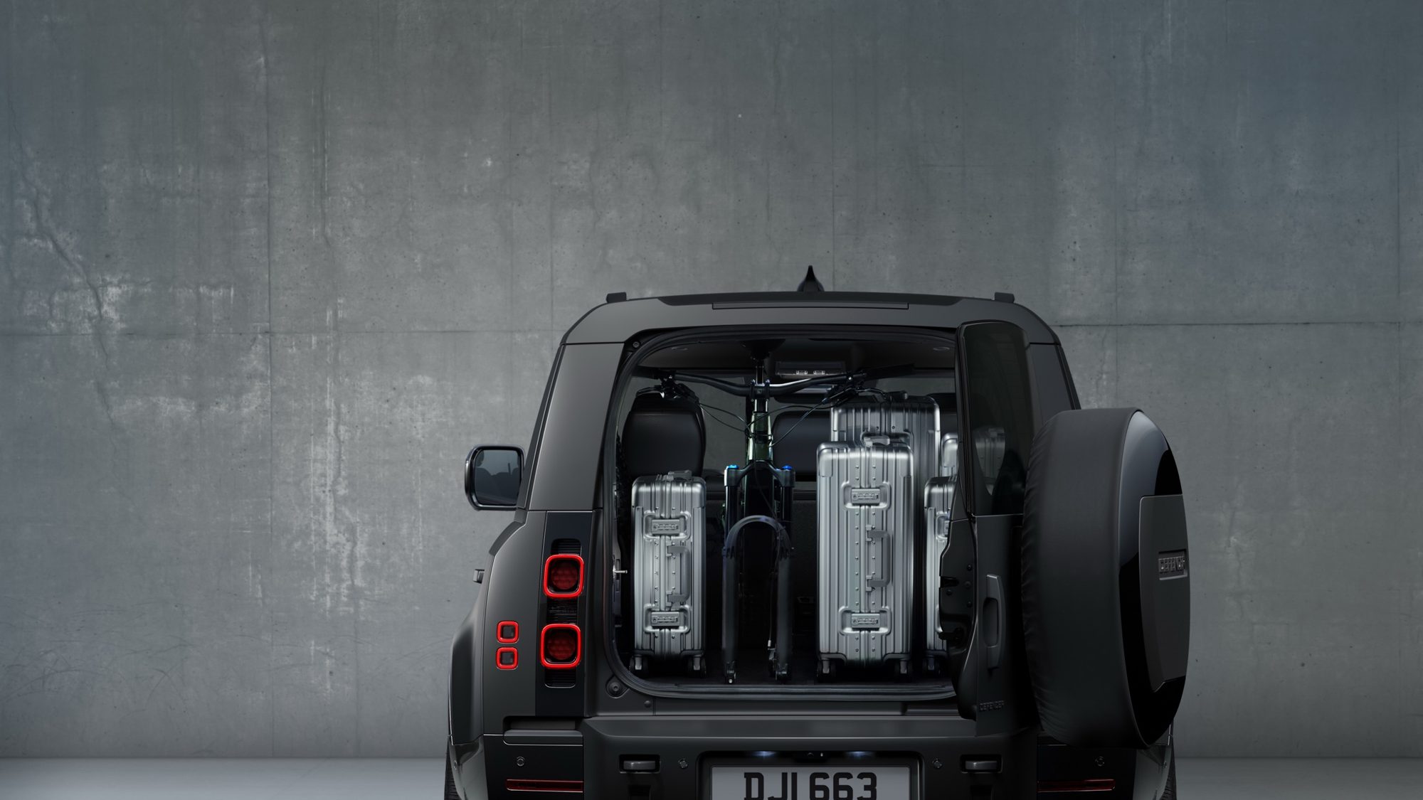Open rear door of the 2024 Land Rover Defender 130 Outbound showing luggage and a bicycle in the cargo area
