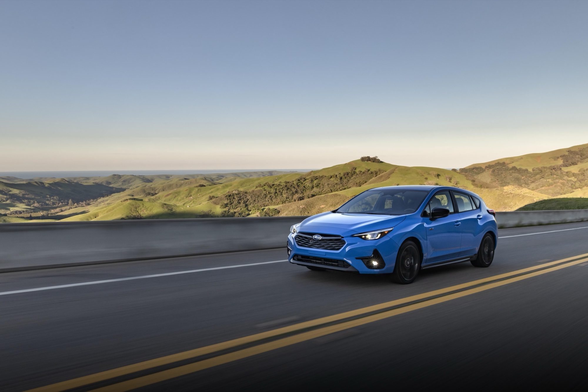 Blue 2024 Subaru Impreza RS driving on a coastal hill road