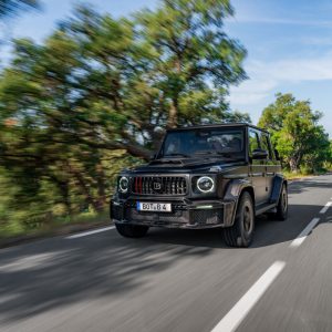 Black Brabus 900 Rocket Edition Cabrio driving on a tree-lined road, front three-quarter view with the soft top closed