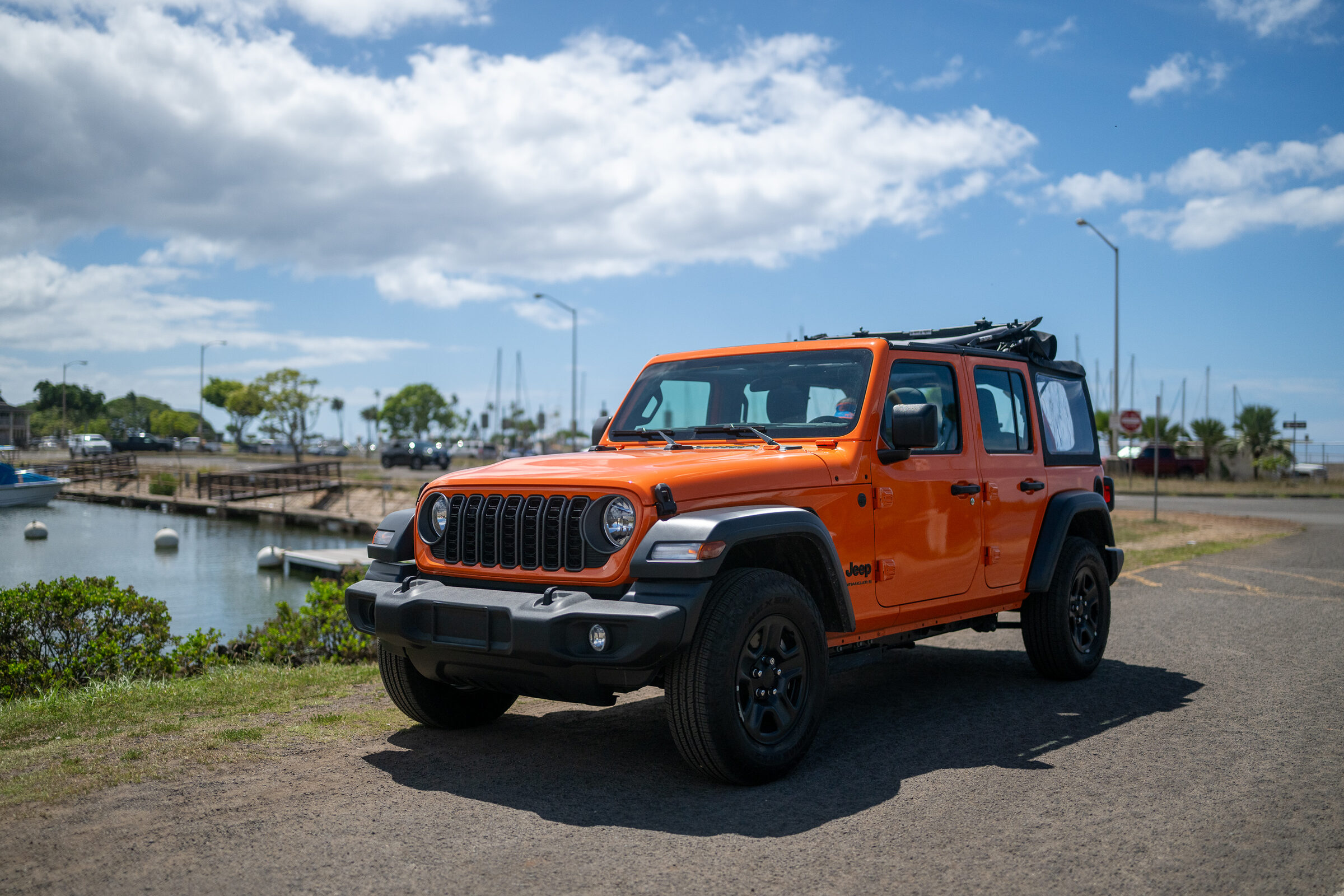 2026 Jeep Wrangler Sport 4-door in Joose orange at Haleiwa Boat Harbor with the soft top folded into the Sunrider position