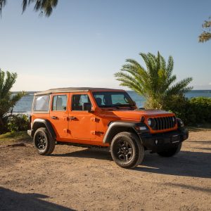 2026 Jeep Wrangler Sport 4-door in Joose orange with its soft top up beside the ocean on Oʻahu's North Shore