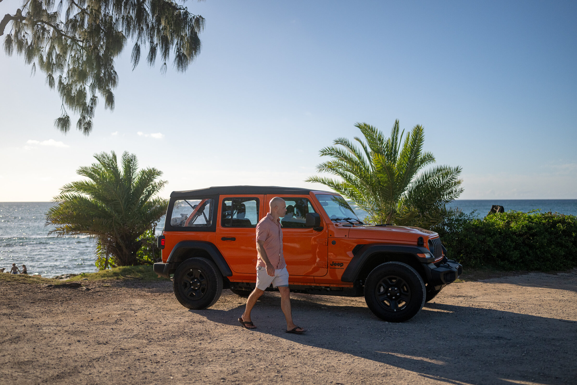 Michael Kahn walking past a 2026 Jeep Wrangler Sport 4-door in Joose orange with its soft top raised on Oahu's North Shore