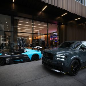 Dark gray Toyota Century on black wheels parked beside a Dallara race car outside The Department at Hudson's in Detroit