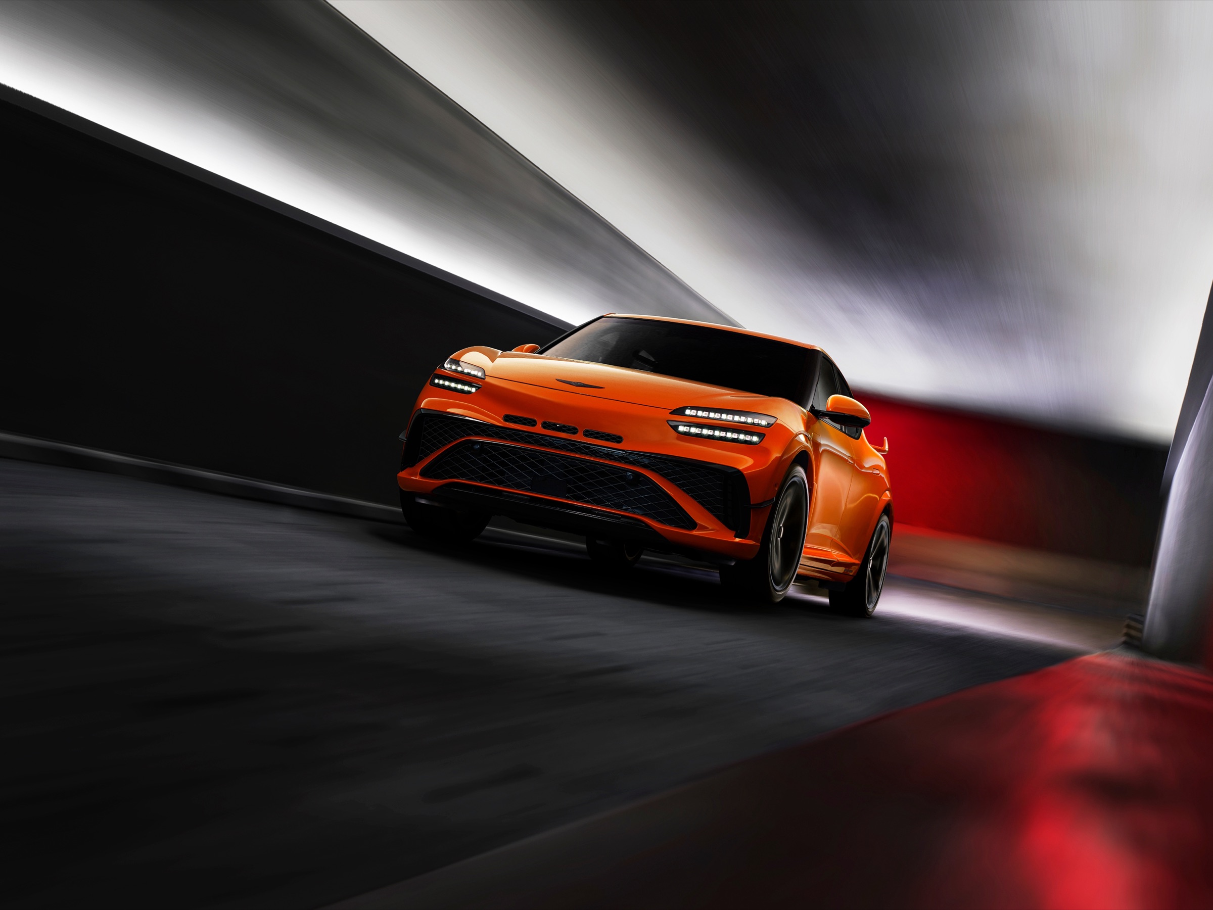 Orange Genesis GV60 Magma driving through a dark set with streaks of light, front three-quarter view