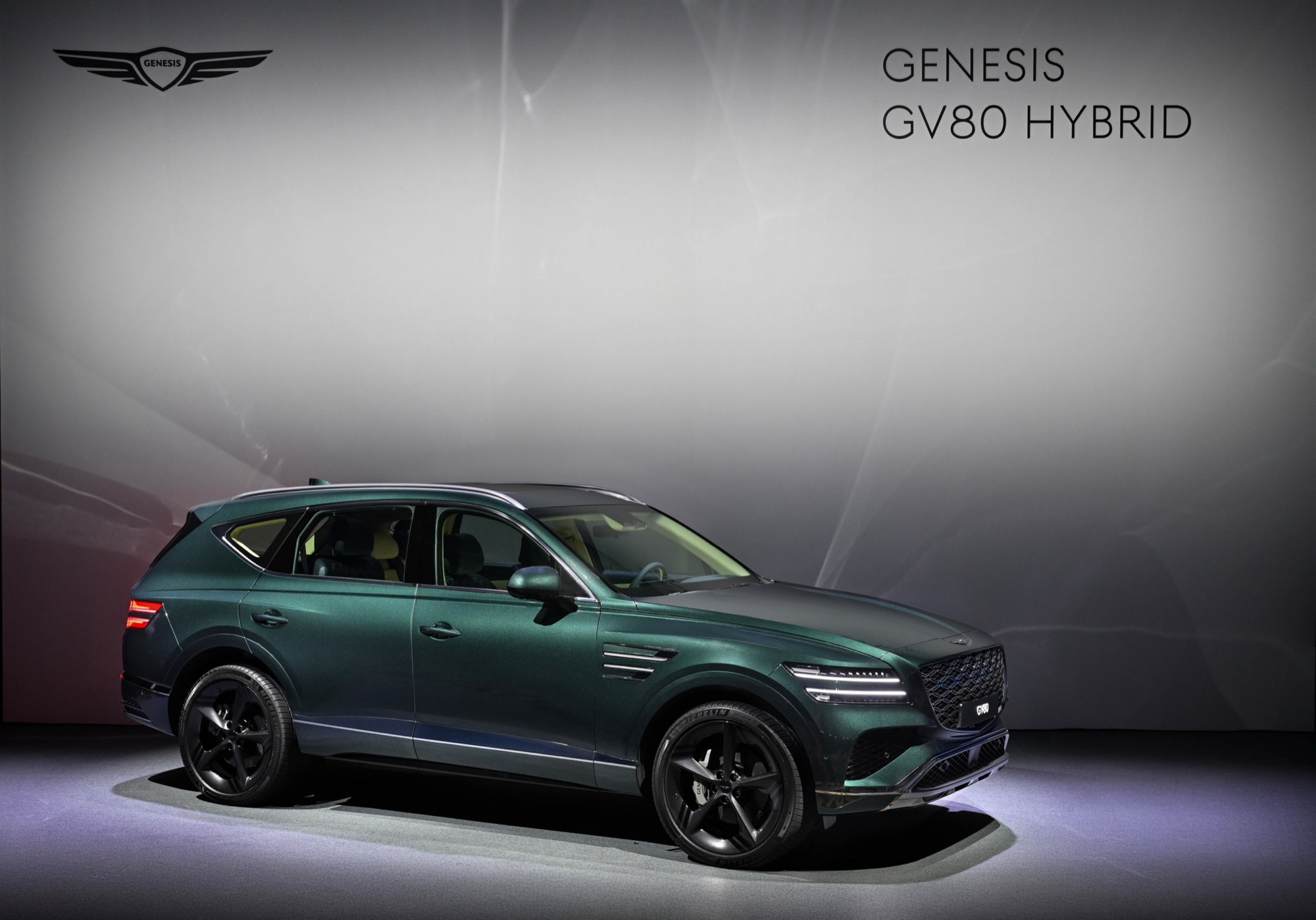 Dark green Genesis GV80 Hybrid on black wheels displayed on stage under a Genesis GV80 Hybrid sign