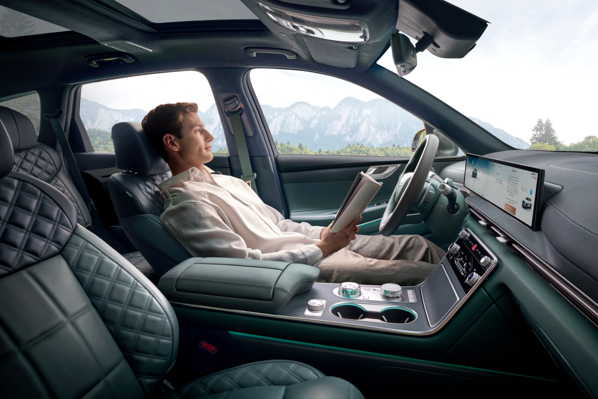 Driver reclined and reading in the front seat of a parked Genesis GV80 Hybrid with green leather interior