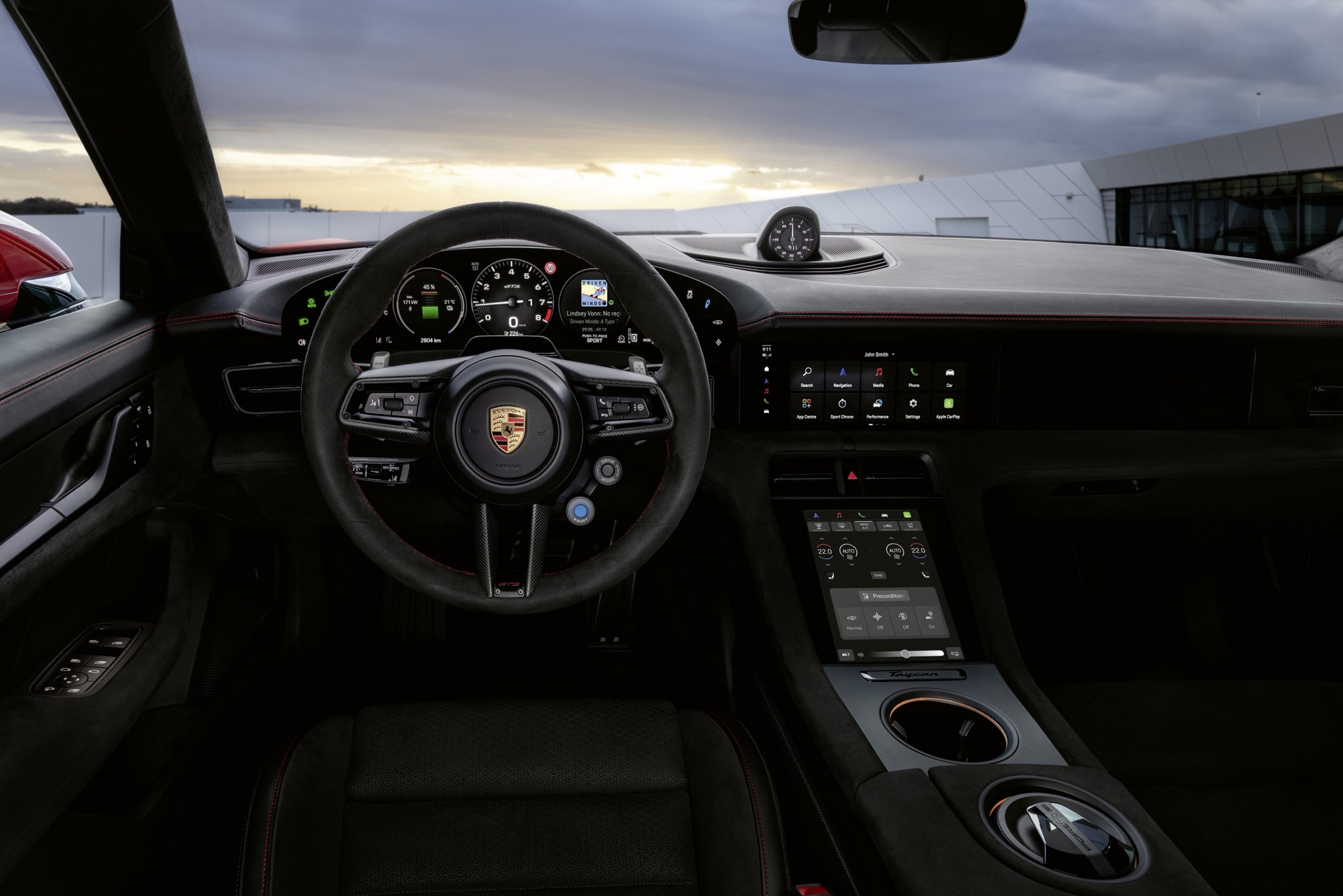 Porsche Taycan GTS cockpit at dusk showing steering-wheel paddles, the E-Shift button and an analog-style rev counter