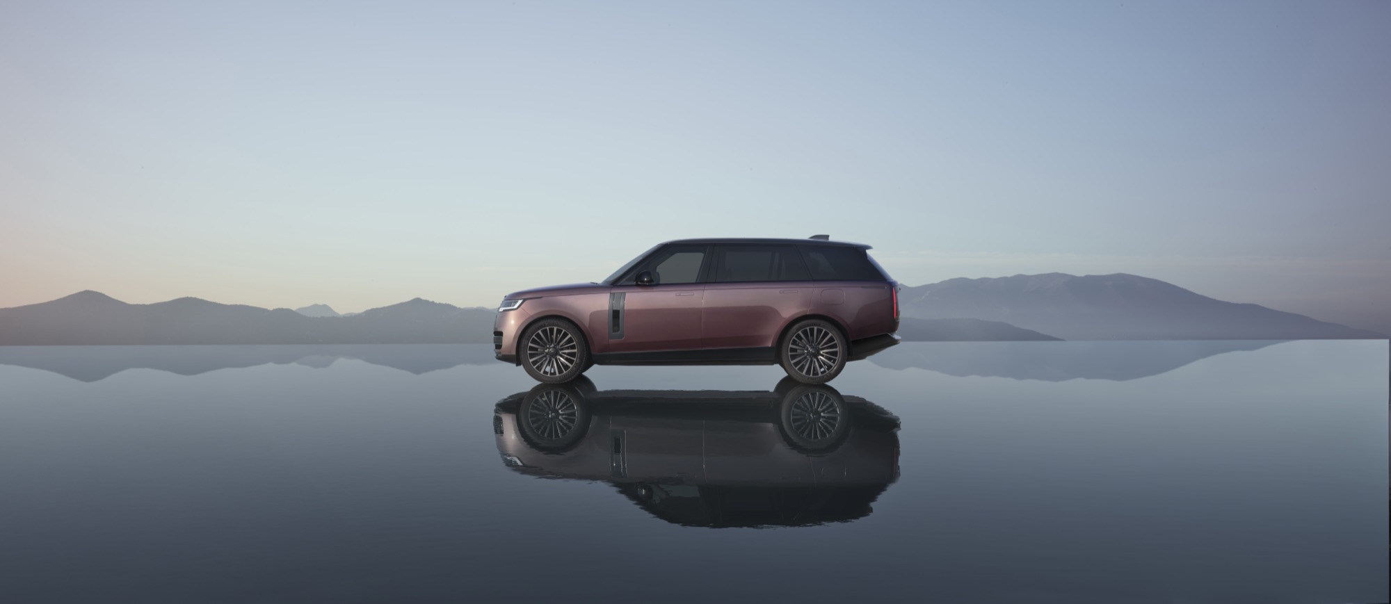 Range Rover Electric Starts at $138,000, the Same Price as the V8 SE 3 Range Rover Electric in a two-tone red and dark finish, side profile, reflected in still water