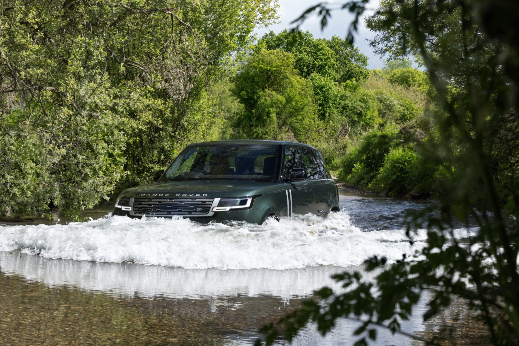 Dark green Range Rover Electric driving through a river crossing with water at bumper height