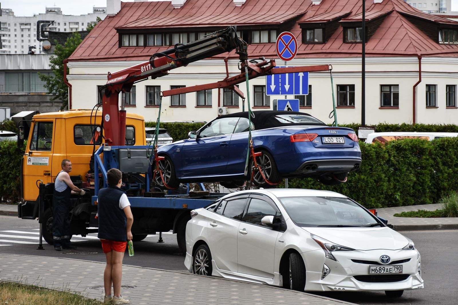 Tow truck crane lifting a blue convertible off a city street