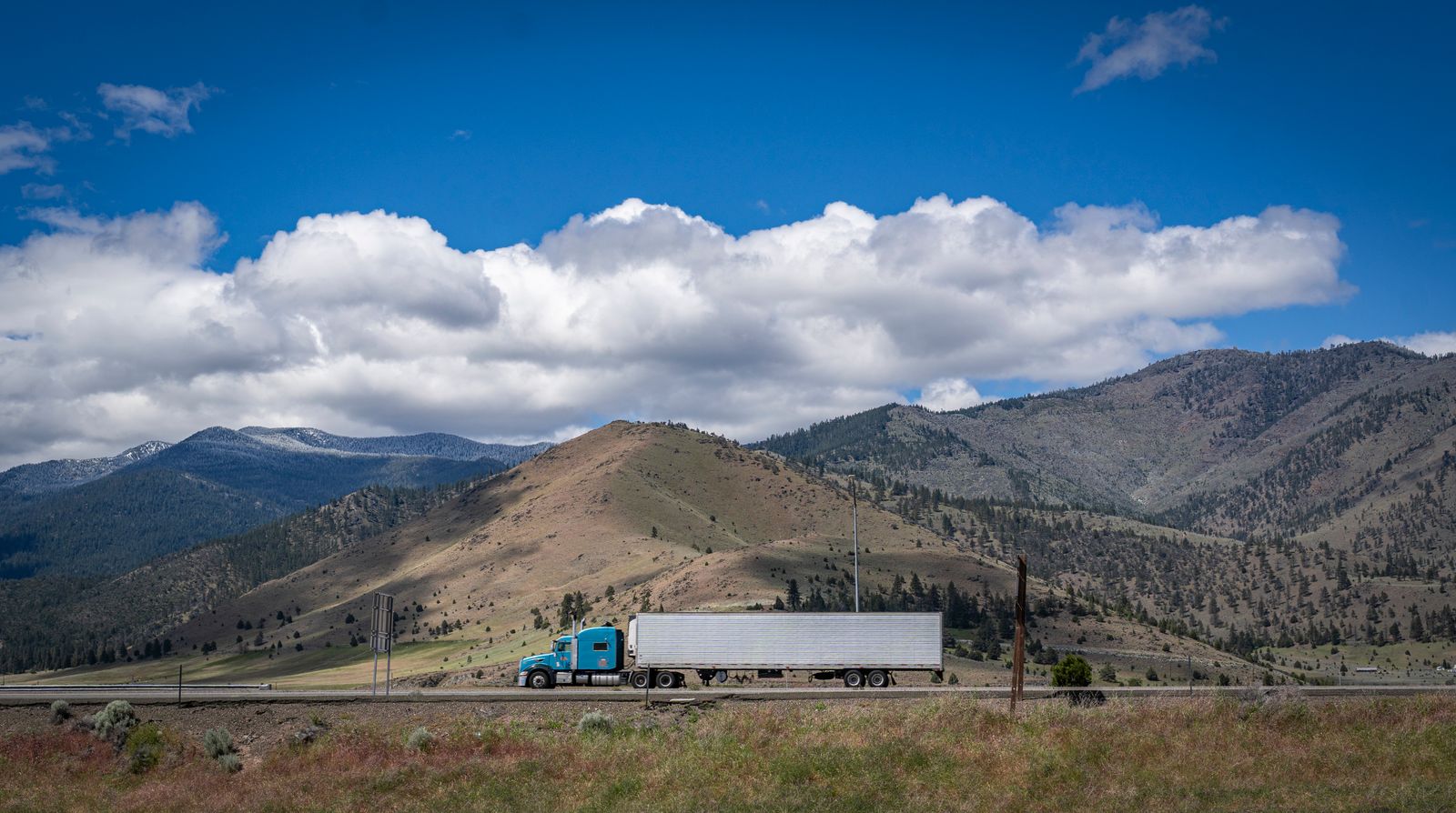 Blue semi truck on a highway below mountains