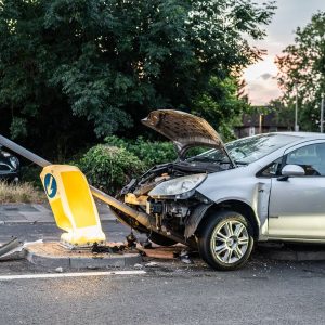 Silver hatchback with front-end damage after hitting a lamp post