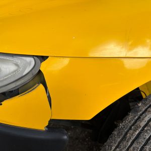 Cracked front bumper and fender on a yellow car after a collision