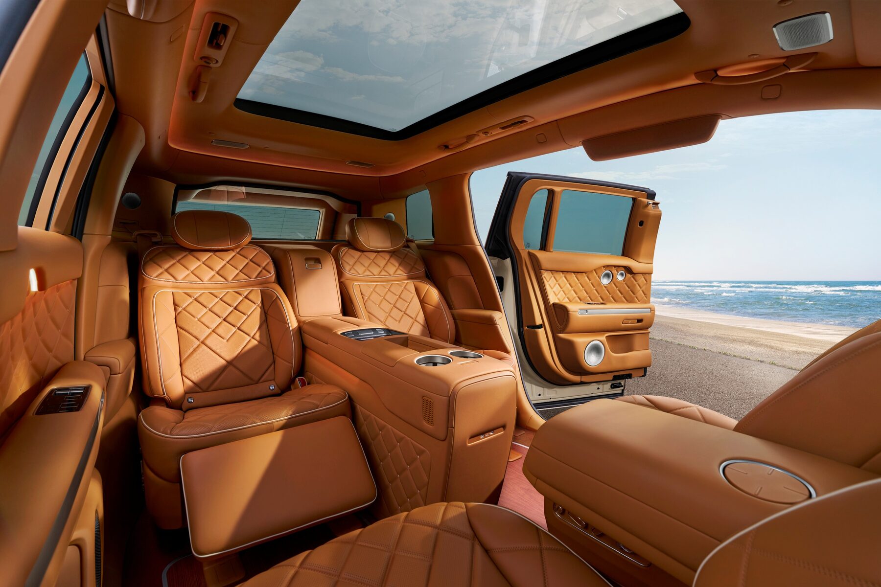 Tan quilted leather rear cabin of the Genesis GV90 Neolun with two individual seats, a center console and the rear-hinged door open to a beach