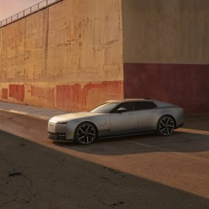 2027 Jaguar Type 01 electric GT in Visionary Silver, front three-quarter view, parked beside a weathered concrete wall